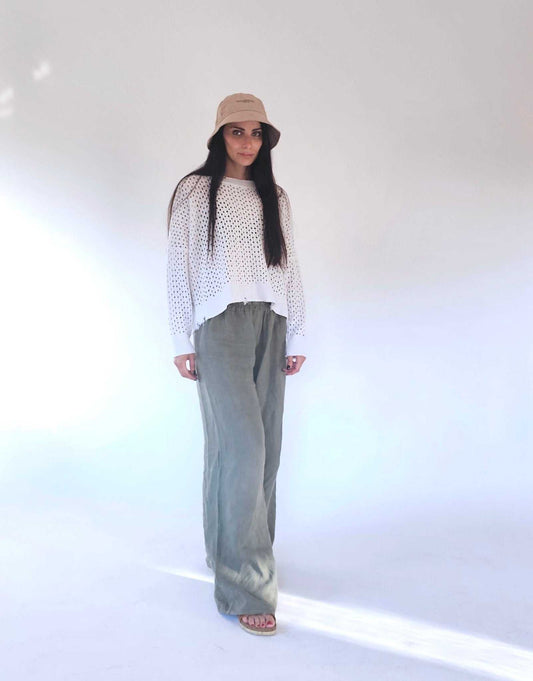 White open-knit cotton sweater by Tenné with fringed hem, paired with relaxed green trousers. Ideal for spring/summer layering.