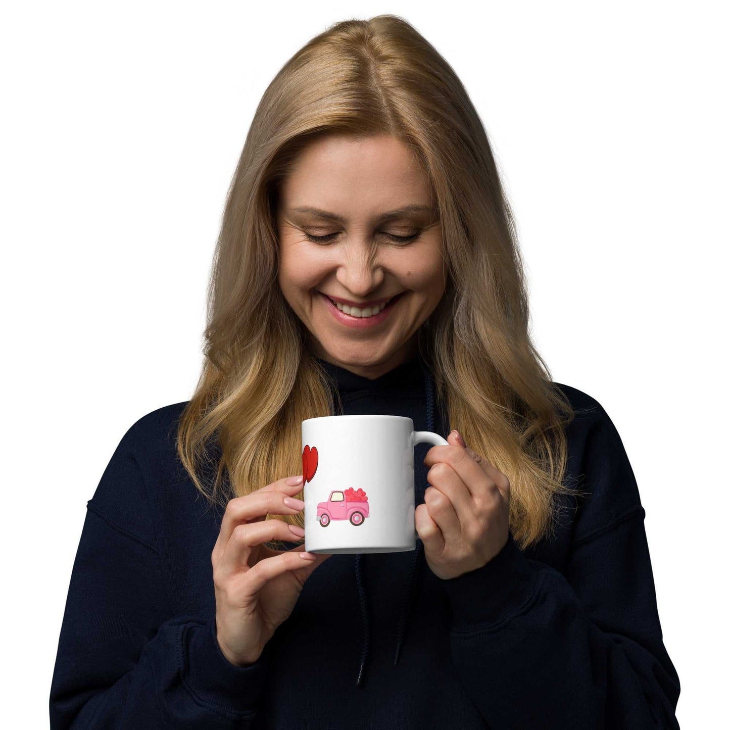 Woman smiling while holding Valentine mug with pink truck and hearts, 11 oz ceramic ideal for love-themed gifts.