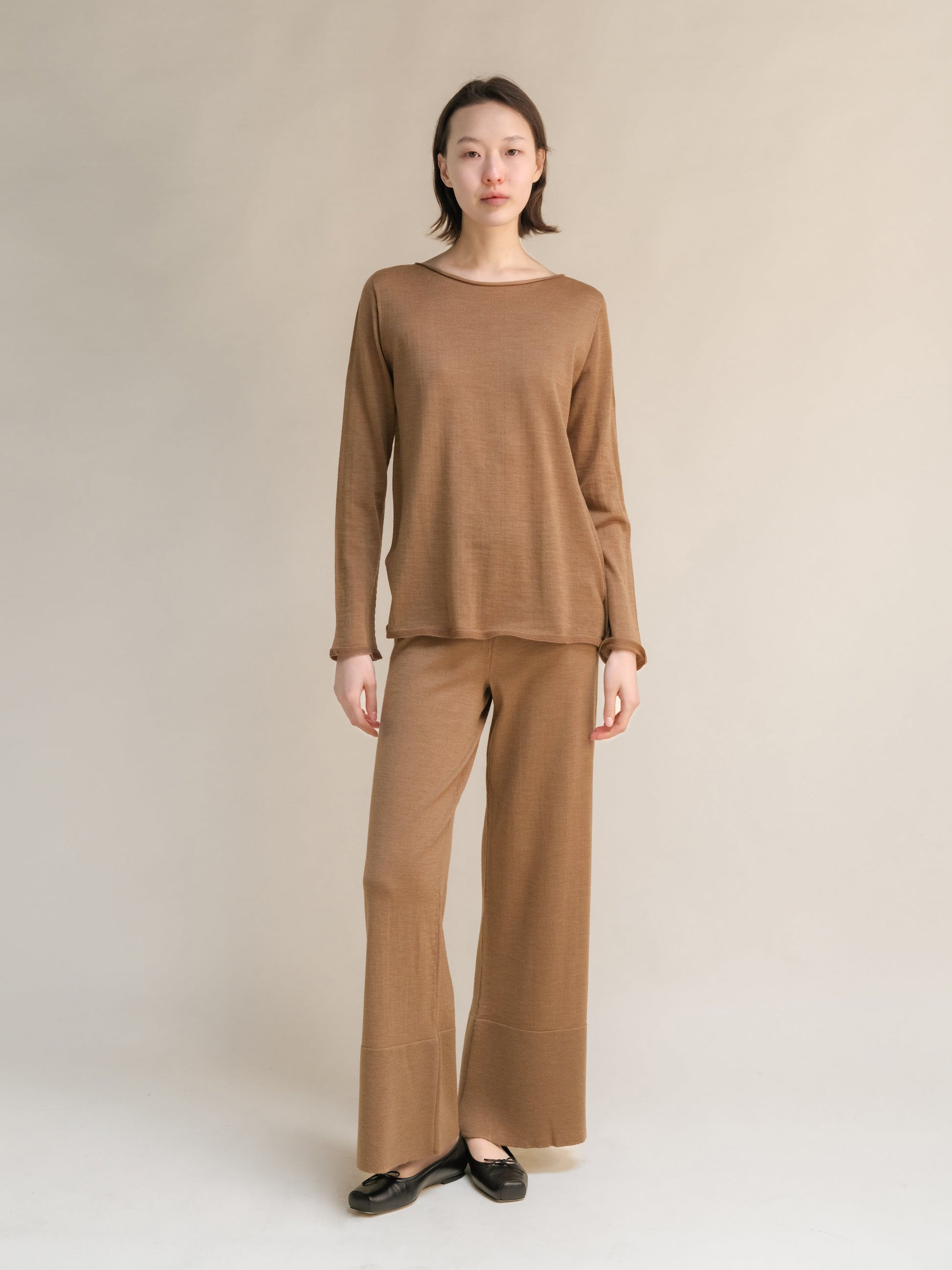 Woman in neutral-toned, long-sleeve knit top and wide-leg pants, minimalist background