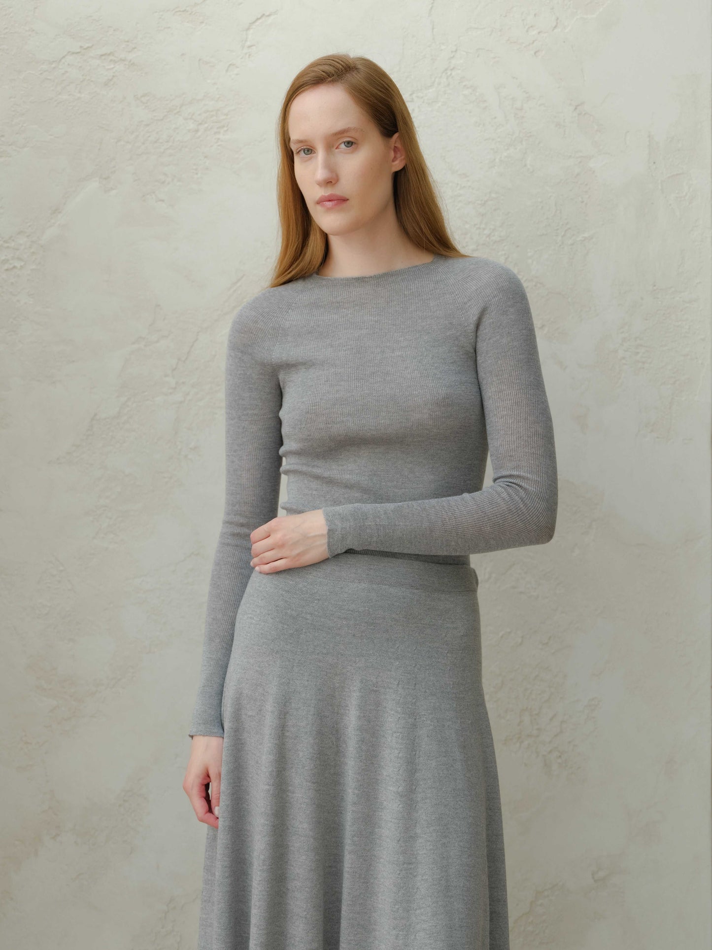 Gray slim fit ribbed crewneck in extra fine merino wool, styled with matching skirt. Breathable and warm knitwear for refined everyday wear.