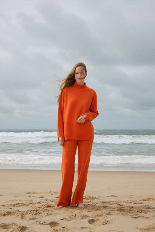 Woman wearing an orange outfit standing with bear feet on a windy beach
