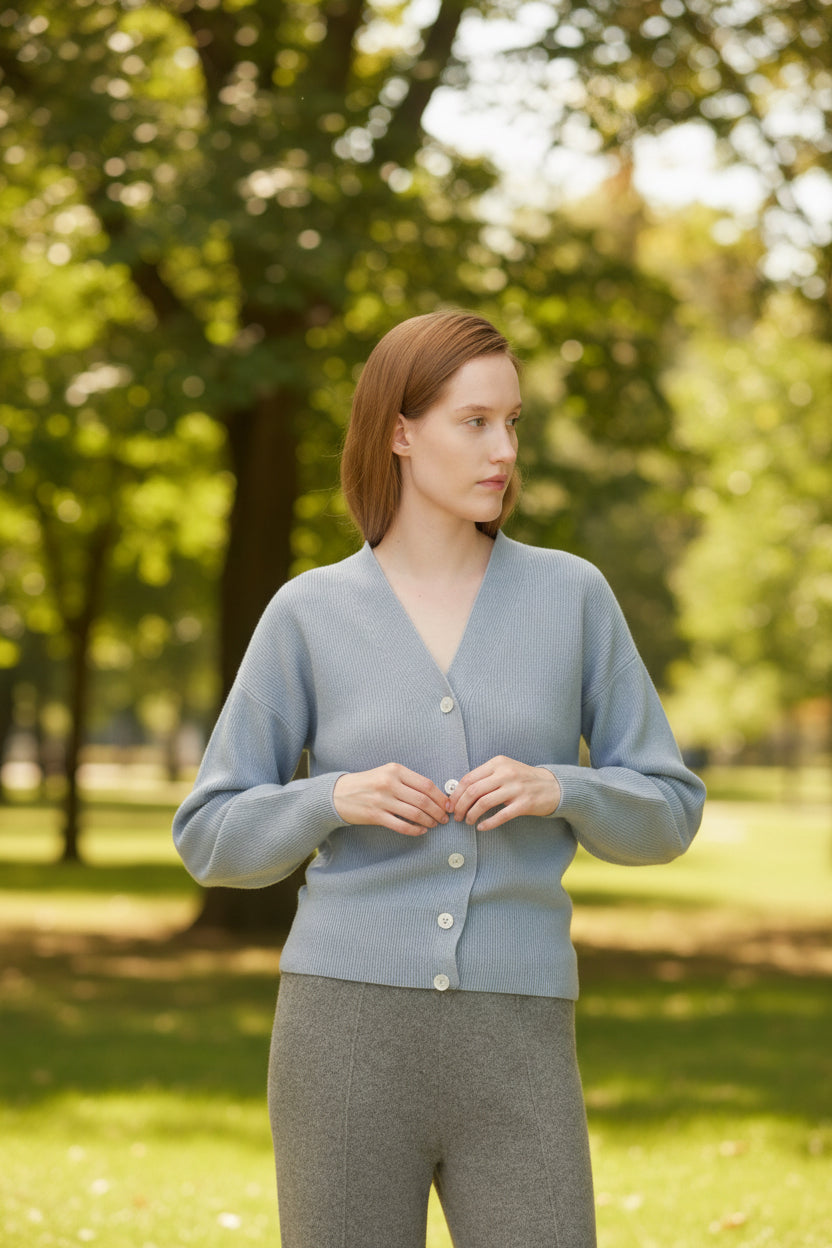 Woman wearing a light blue cardigan and gray pants against a neutral background