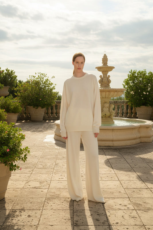 Person wearing a beige sweater and pants against a fountain in the back