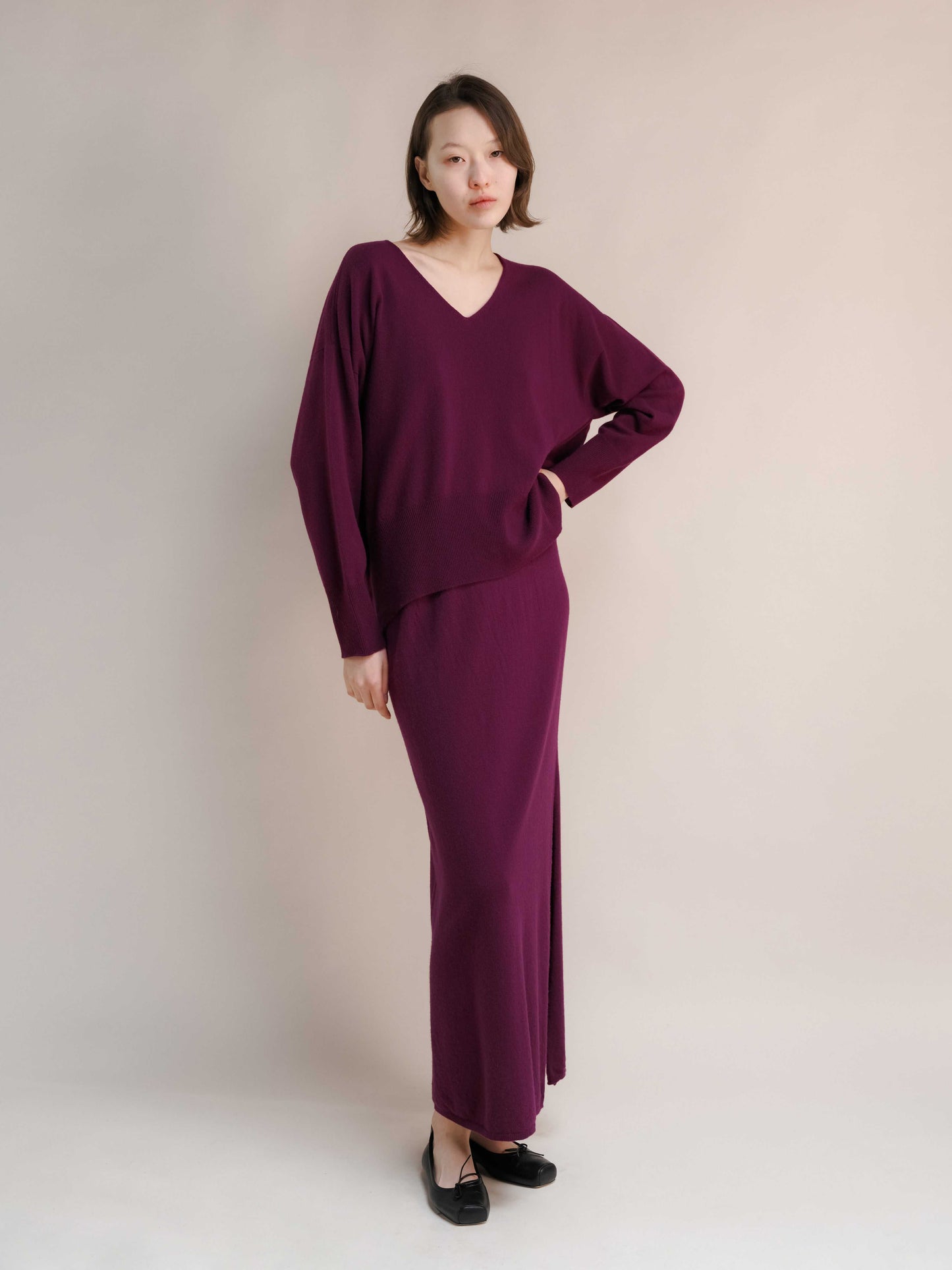 Cashmere skirt with side slit in plum, paired with relaxed V-neck knit top. Premium Italian knitwear for stylish everyday wear.