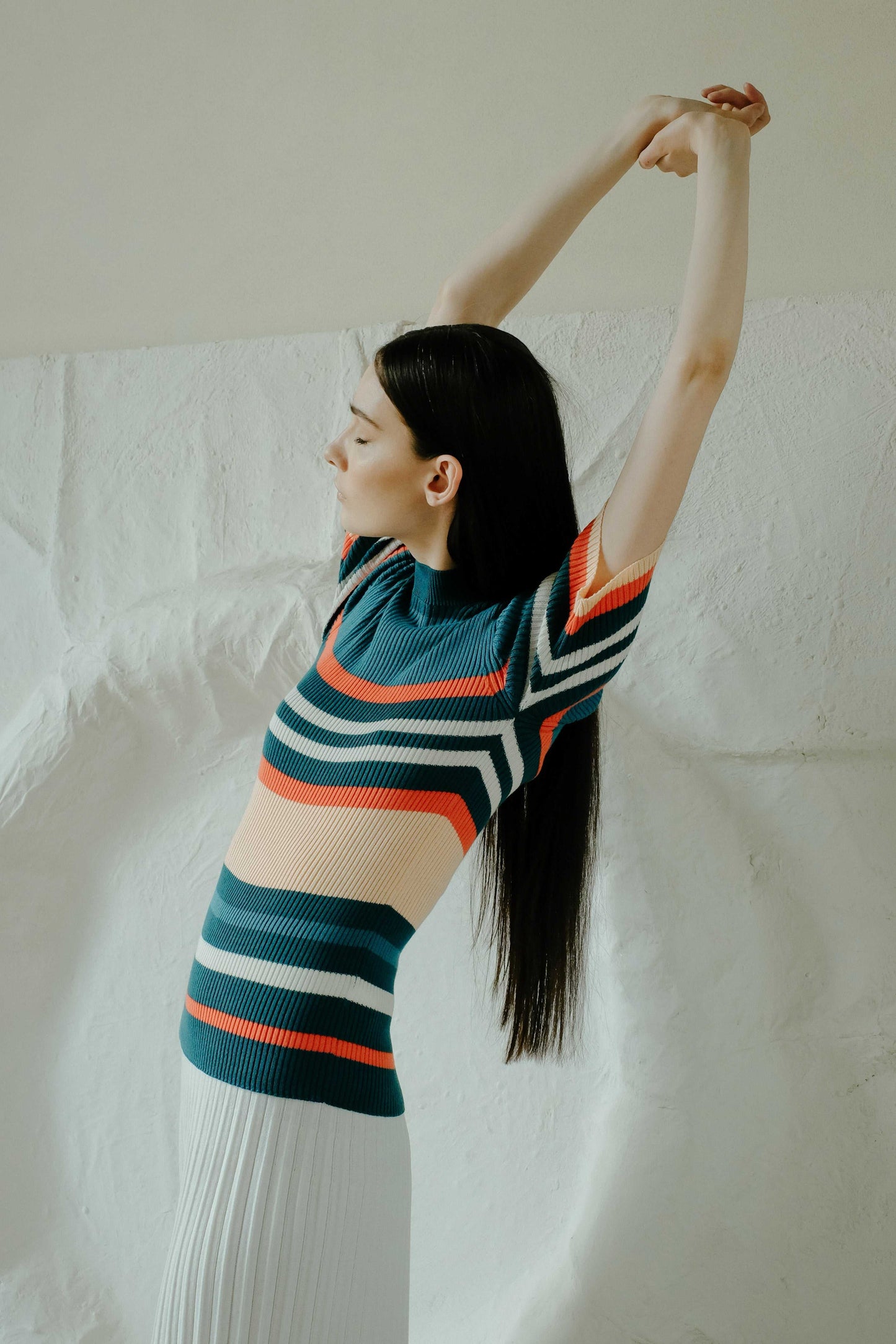 Model stretching in dark teal and coral striped Pima cotton ribbed t-shirt, part of HenryPawHaven's Italian Summer Knitwear collection.