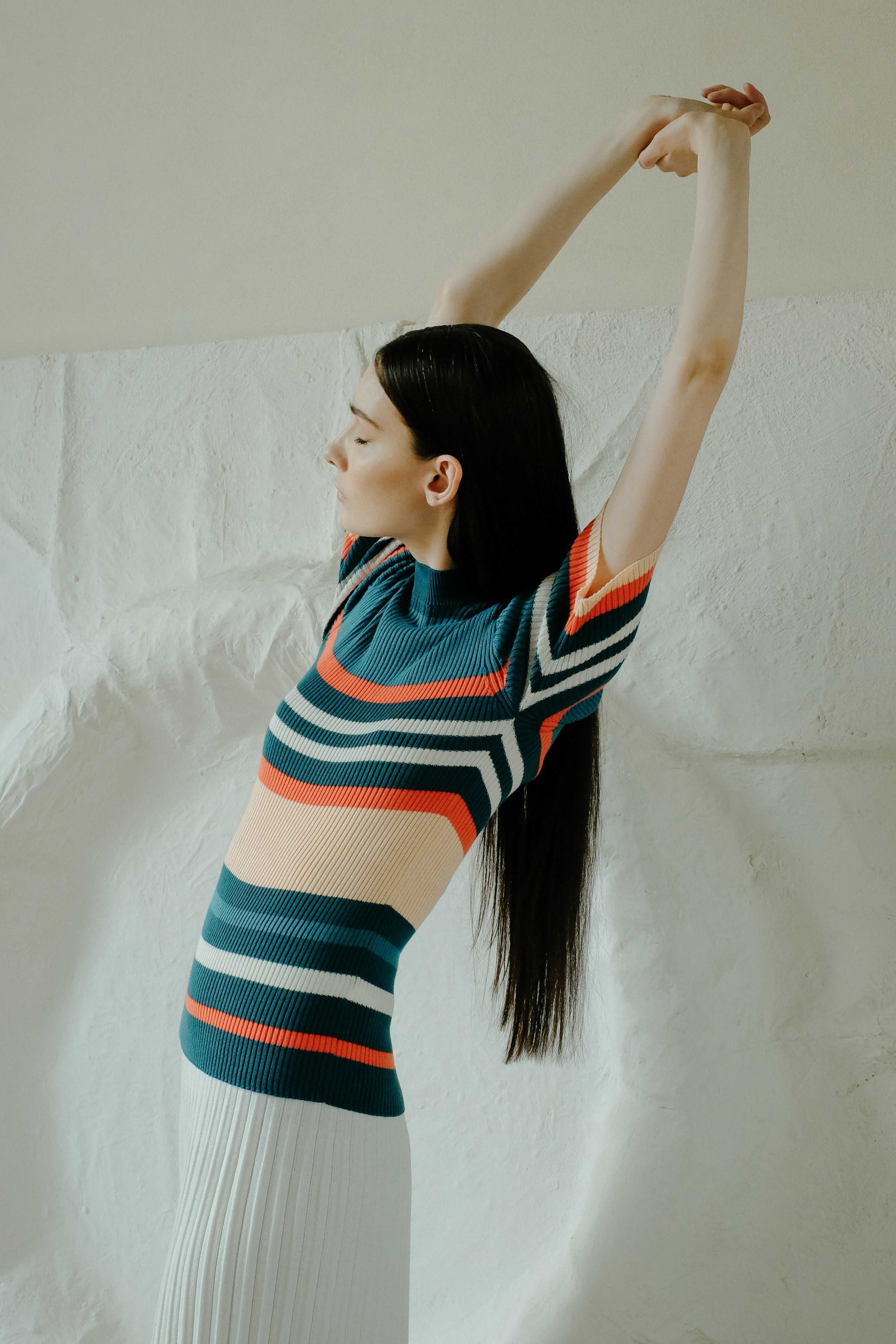 Model stretching in dark teal and coral striped Pima cotton ribbed t-shirt, part of HenryPawHaven's Italian Summer Knitwear collection.