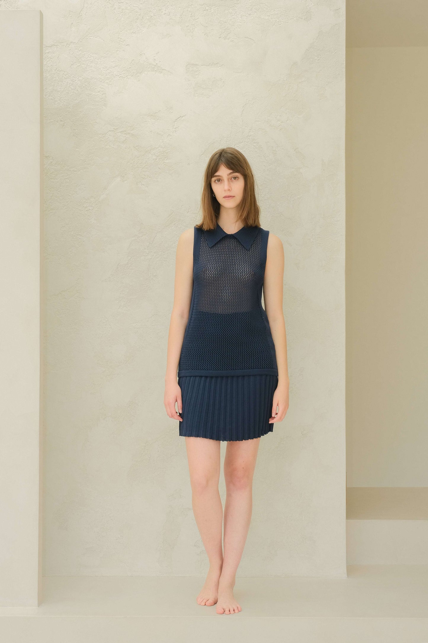 Model in navy plissé mini skirt and knit top