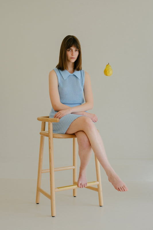 Model seated on wooden stool wearing Fine Crochet Polo Tank Top in blue. Lightweight Italian merino knitwear from HenryPawHaven.
