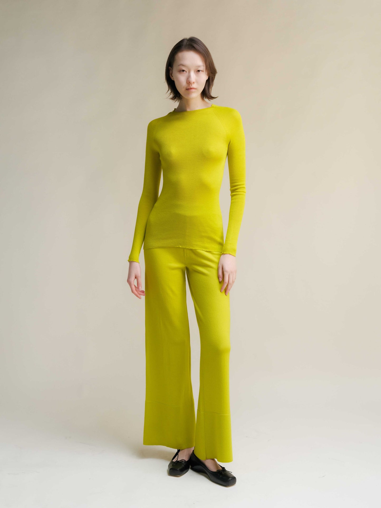 Lime green slim fit ribbed crewneck in extra fine merino wool, styled with matching pants. Vibrant, seamless knitwear for bold fashion statements.