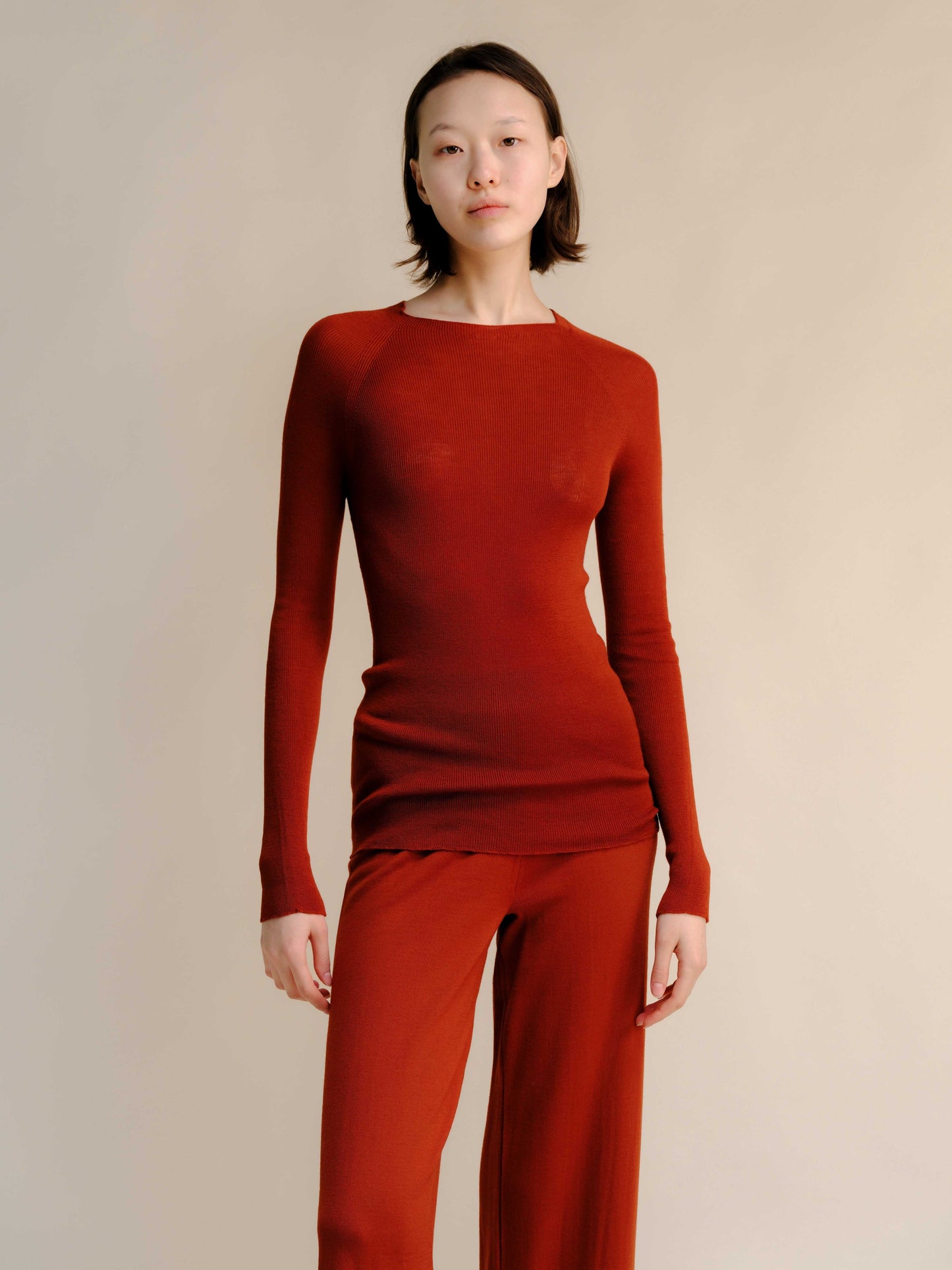 Rust red slim fit ribbed crewneck in extra fine merino wool, paired with matching pants. Seamless, breathable knitwear for warm seasonal style.