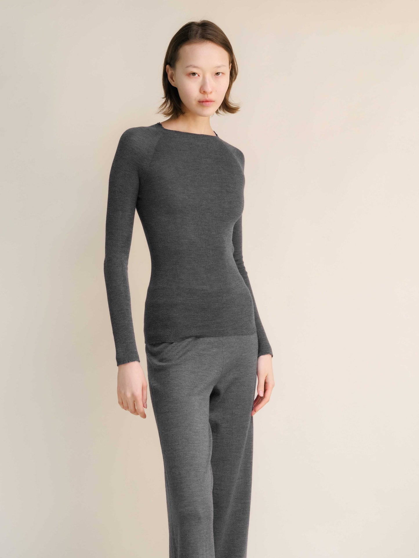 Charcoal gray slim fit ribbed crewneck in extra fine merino wool, styled with matching pants. Seamless, breathable knitwear for everyday elegance.