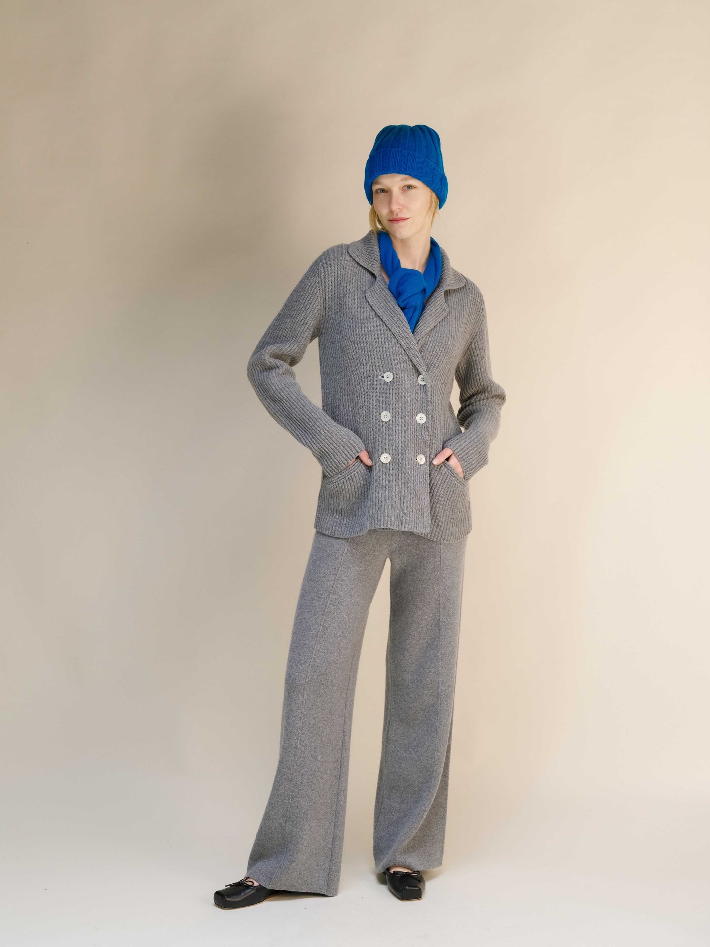 Gray cashmere wool blend double breasted jacket with matching pants, styled with blue accessories for a modern knitwear look.