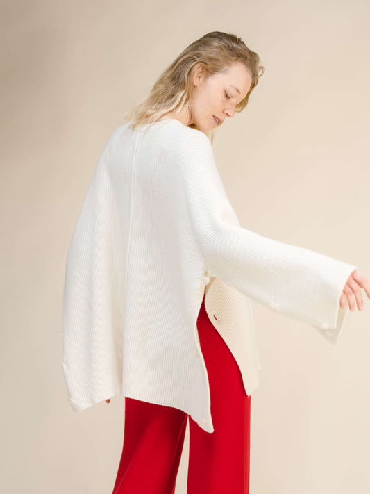 Oversized white cashmere cape sweater with long sleeves and side buttons, Italian craftsmanship by Lèmme at HenryPawHaven, paired with red pants.