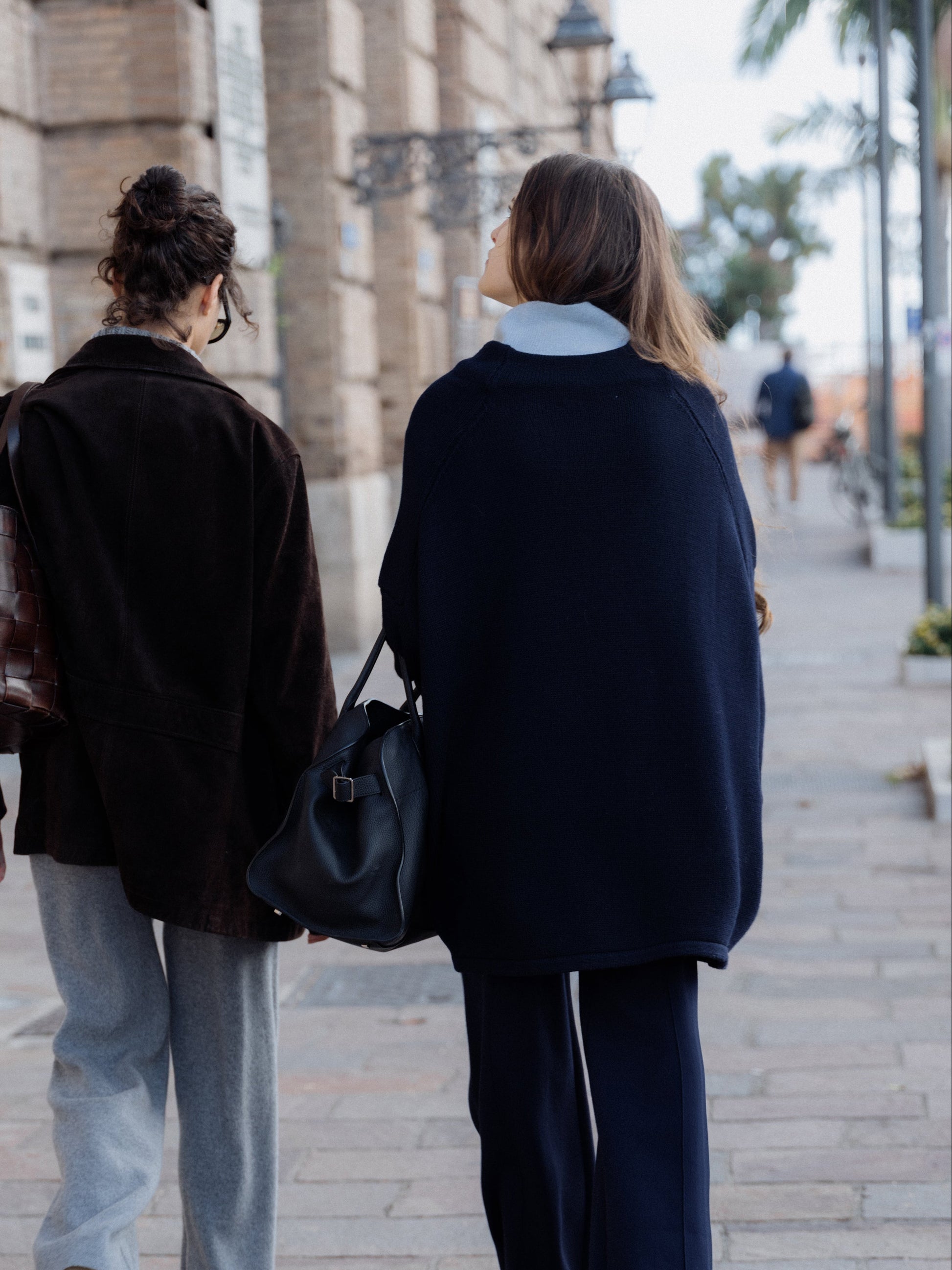 Two people walking on a street in Italy, one carrying a black bag.
