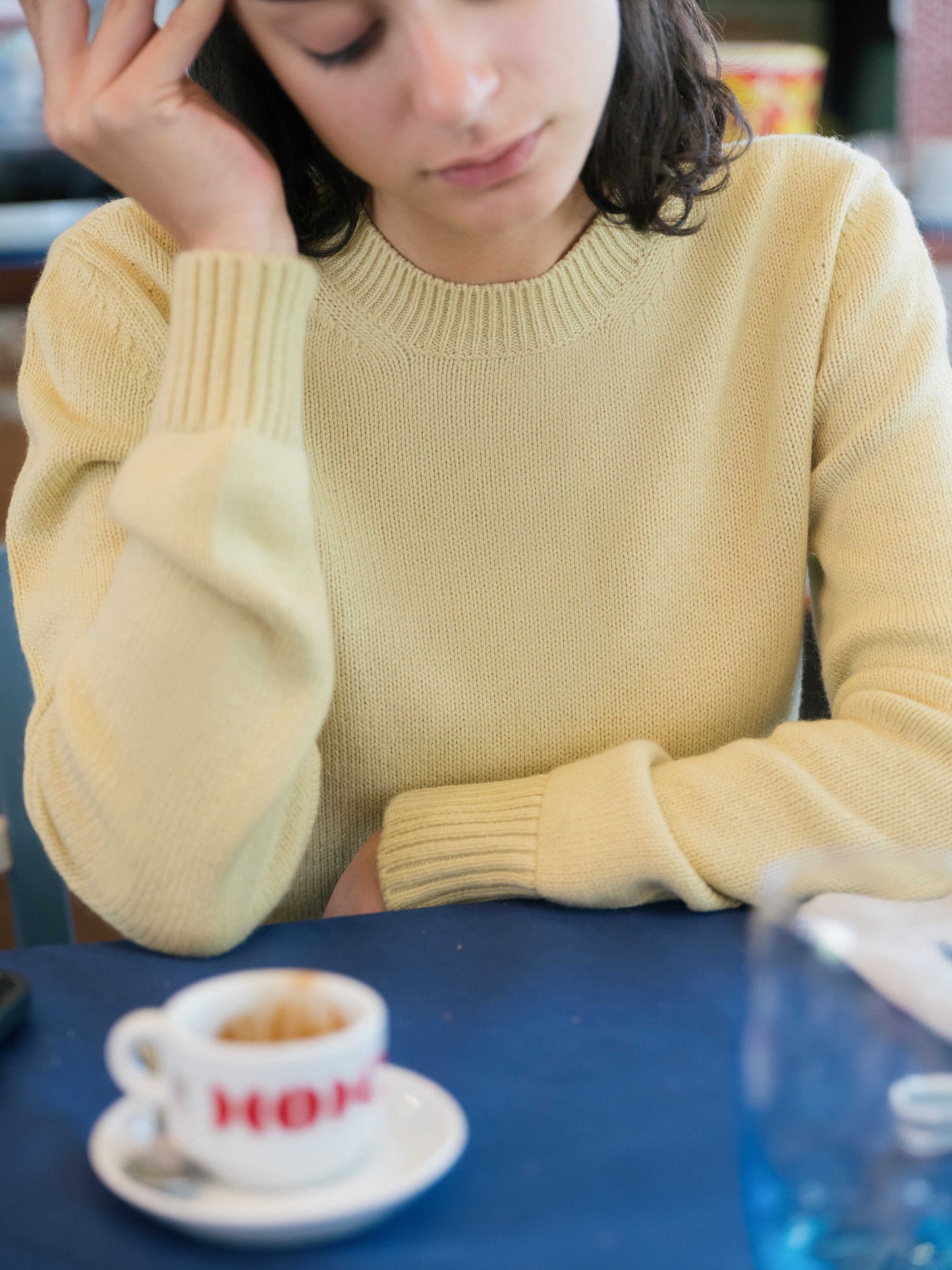 Pure Cashmere Crewneck Sweater in soft yellow worn casually at a café. Luxurious Italian-made knitwear by Lèmme for everyday elegance.
