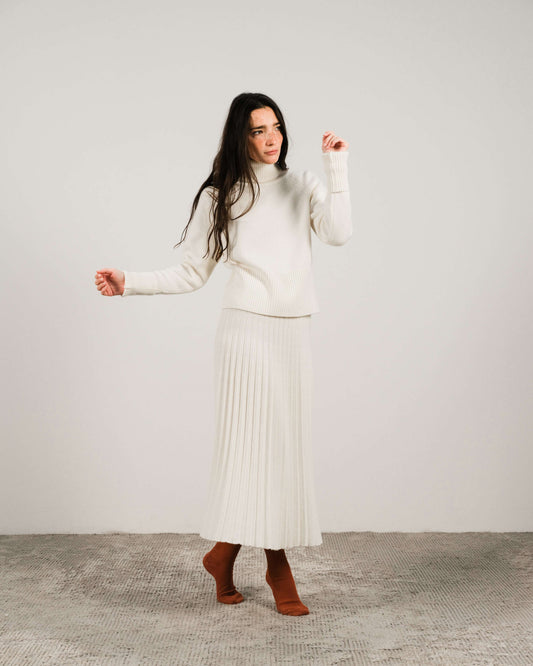 Cashmere turtleneck sweater with roll-up cuffs in ivory, styled with a pleated knit skirt. Italian wool-cashmere blend from HenryPawHaven.