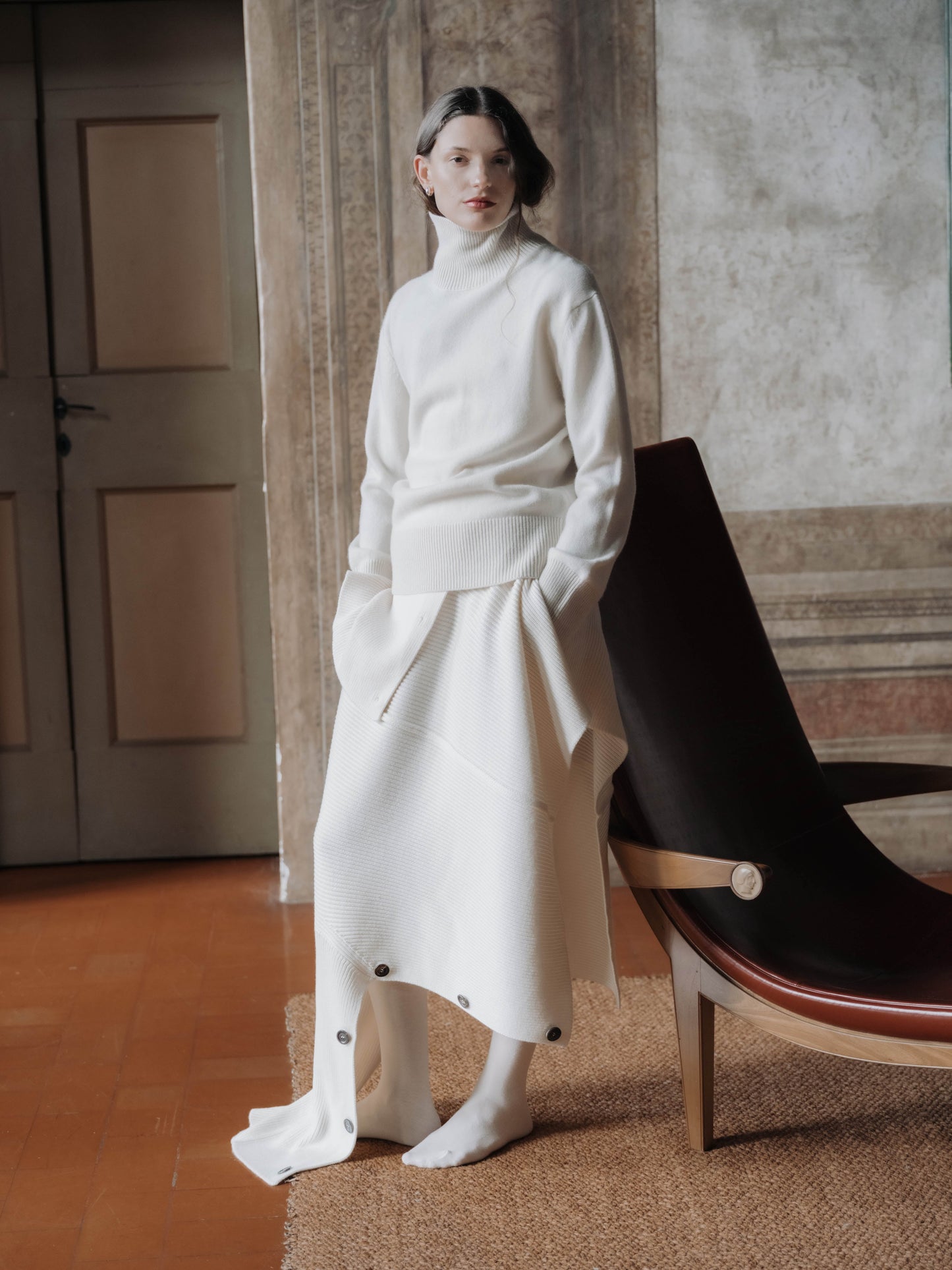 Model wearing full Lèmme ensemble with Extra Fine Merino Convertible Cape Sweater styled as a skirt, showcasing versatile Italian knitwear.