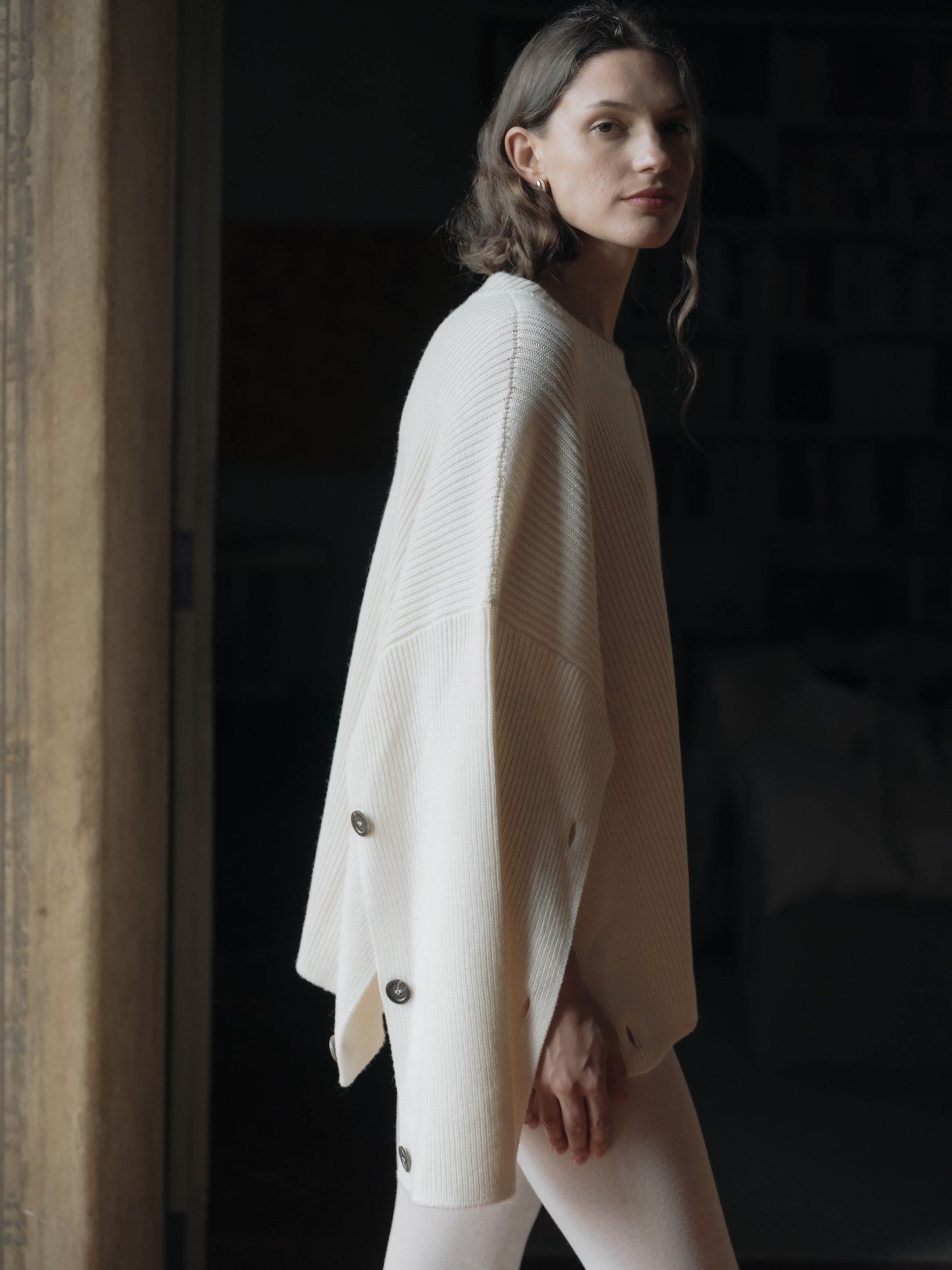 Side profile of Lèmme's Extra Fine Merino Convertible Cape Sweater, featuring ribbed texture and buttoned convertible sleeves.