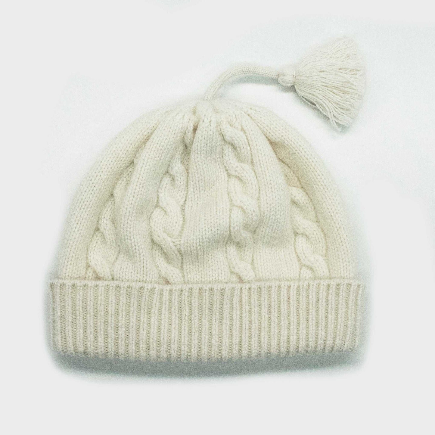 Portolano Baby Cashmere Hat in white with cable knit design and tassel. Soft 100% cashmere hat for infants, ideal for warmth and comfort.