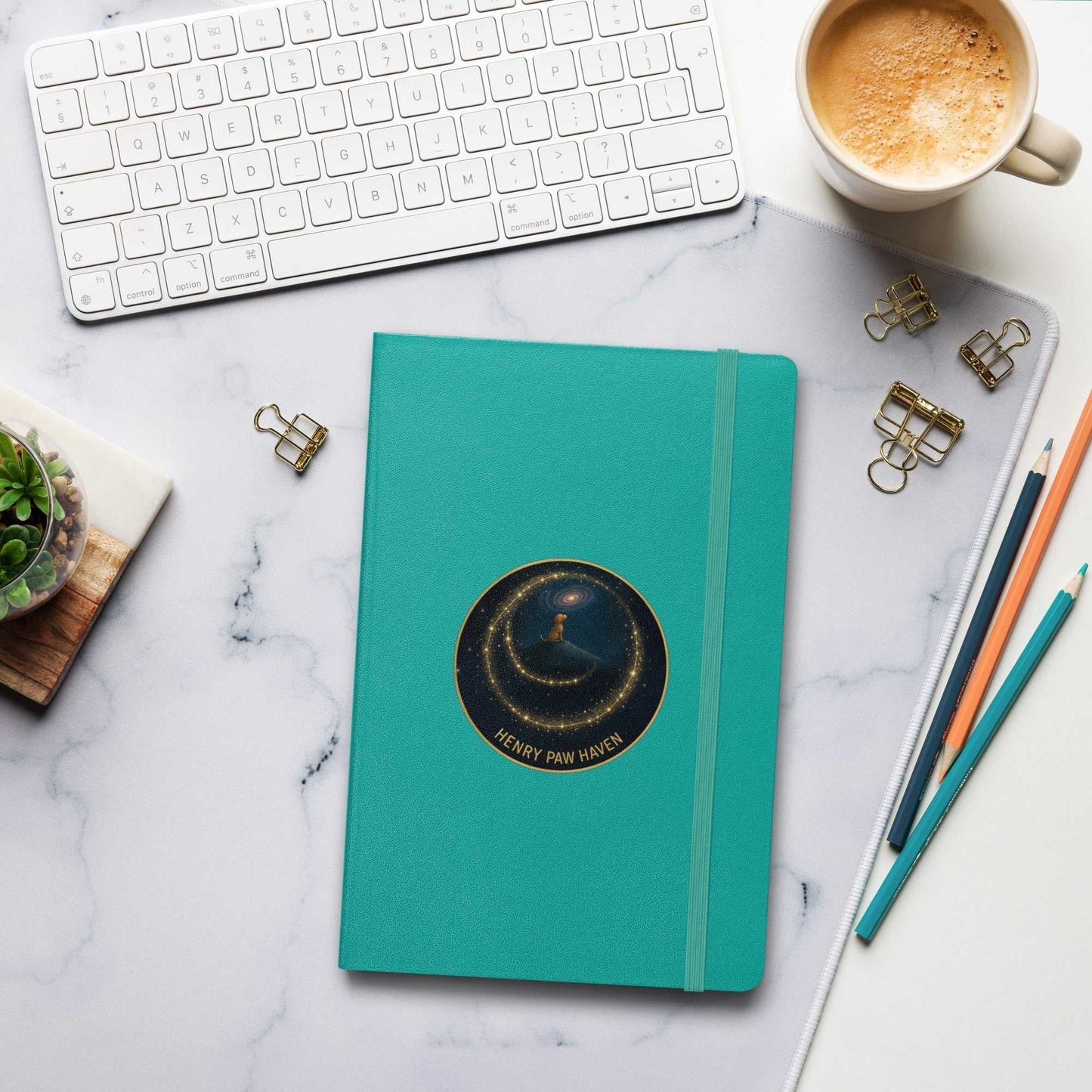 Teal Hardcover Bound Notebook 5.5" × 8.5" with elastic strap and HenryPawHaven logo, placed on a modern desk with coffee and pencils.