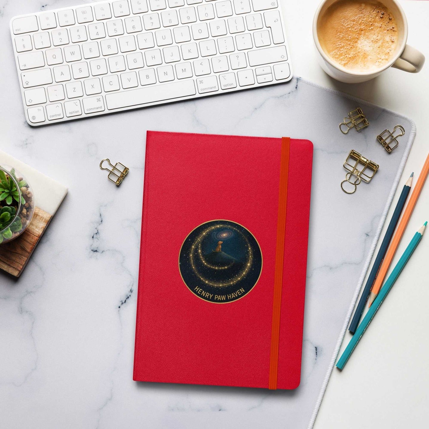 Red Hardcover Bound Notebook 5.5" × 8.5" with elastic strap and HenryPawHaven logo, styled on a marble desk with office accessories.