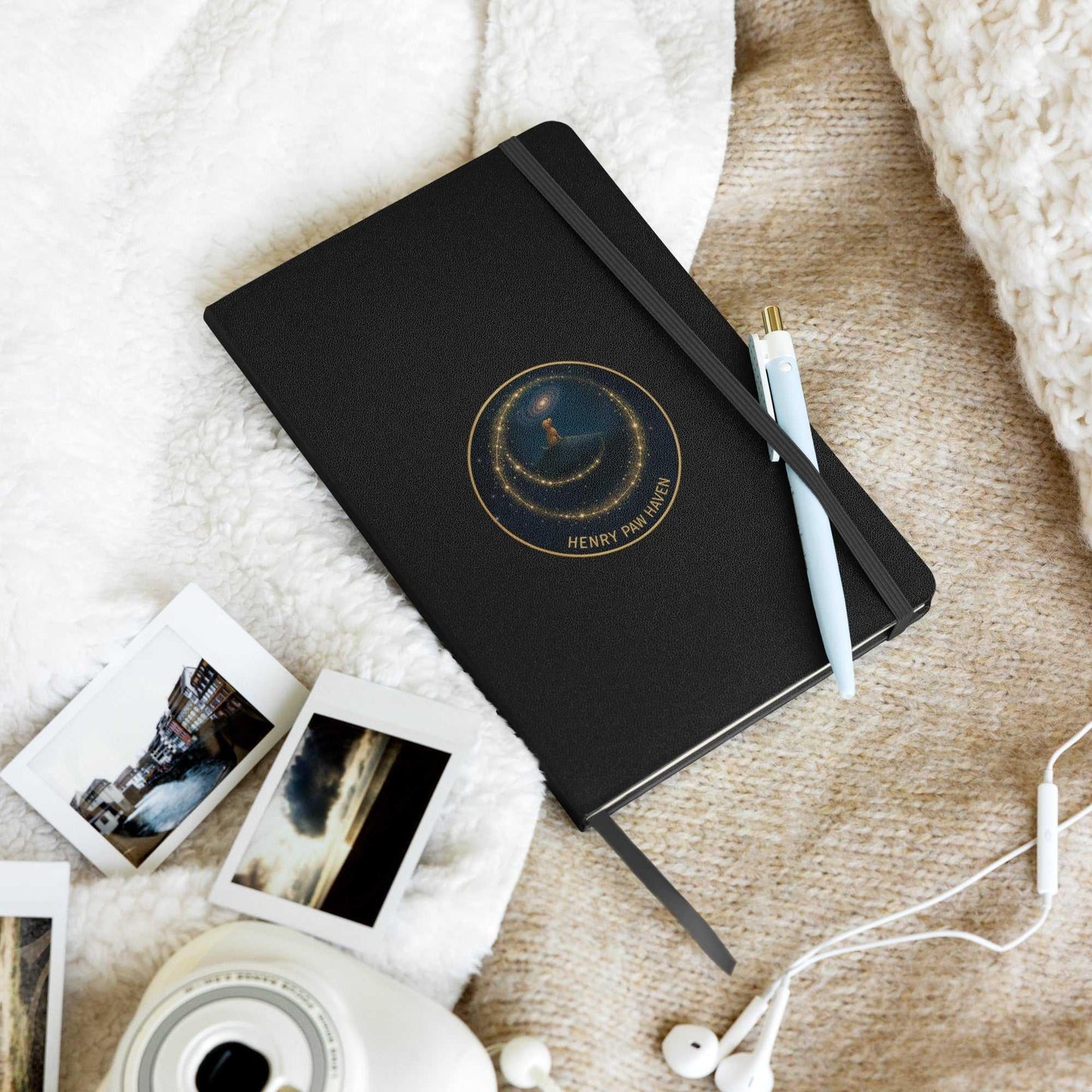 Black hardcover notebook with celestial design, pen, and photos on cozy blanket