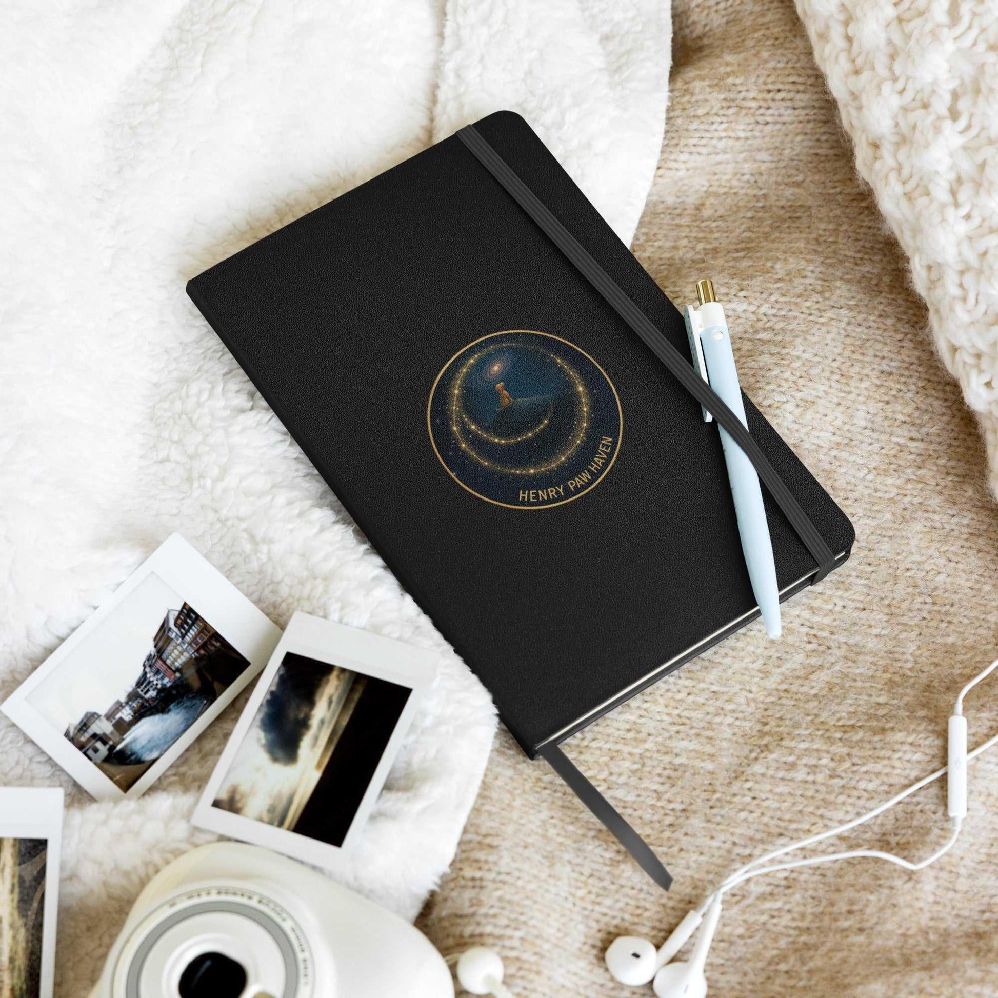 Black hardcover notebook with celestial design, pen, and photos on cozy blanket