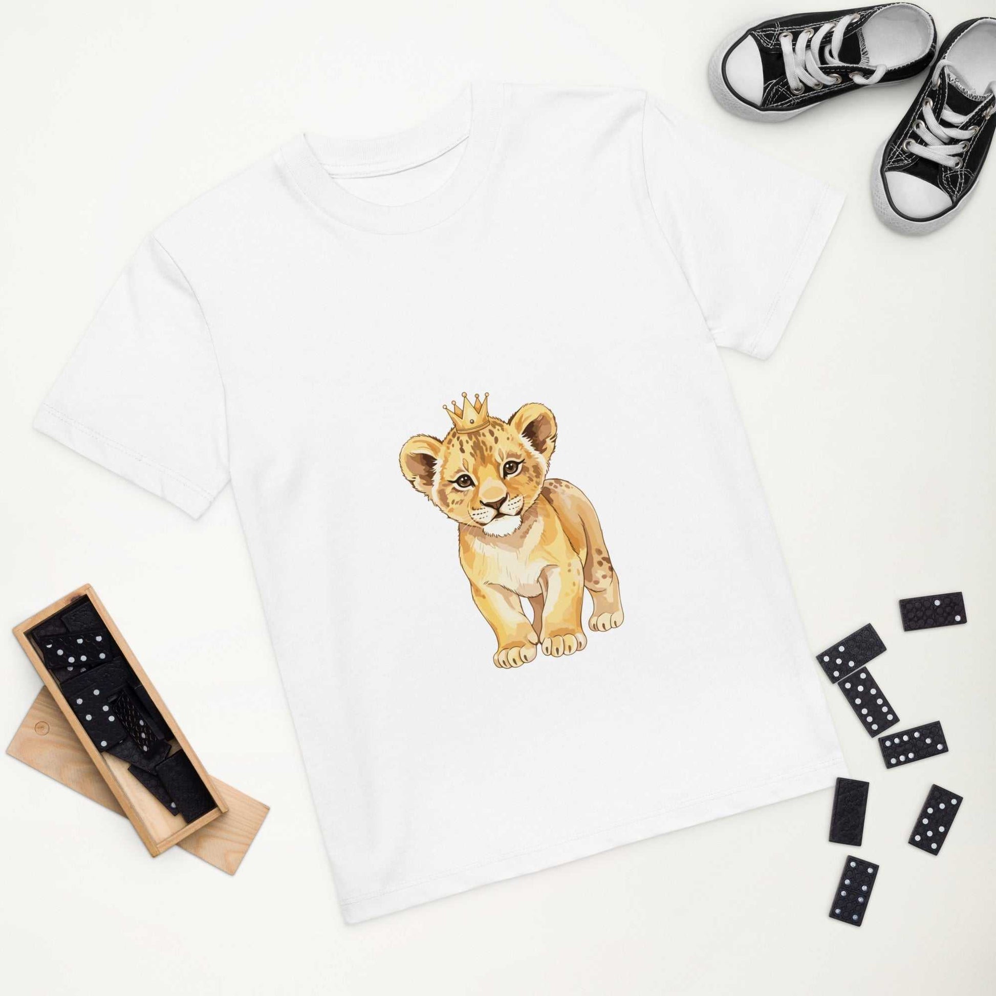 Flat lay of white kids eco t-shirt with baby lion design, surrounded by shoes and toys, made from organic cotton for eco fashion.