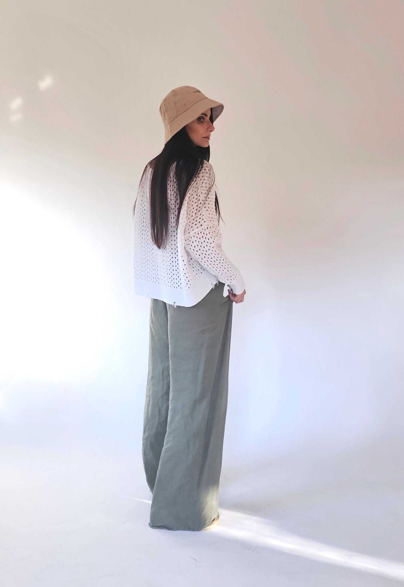 Back view of eco-friendly open-knit cotton sweater by Tenné, styled with loose green pants. Lightweight and breathable spring top.