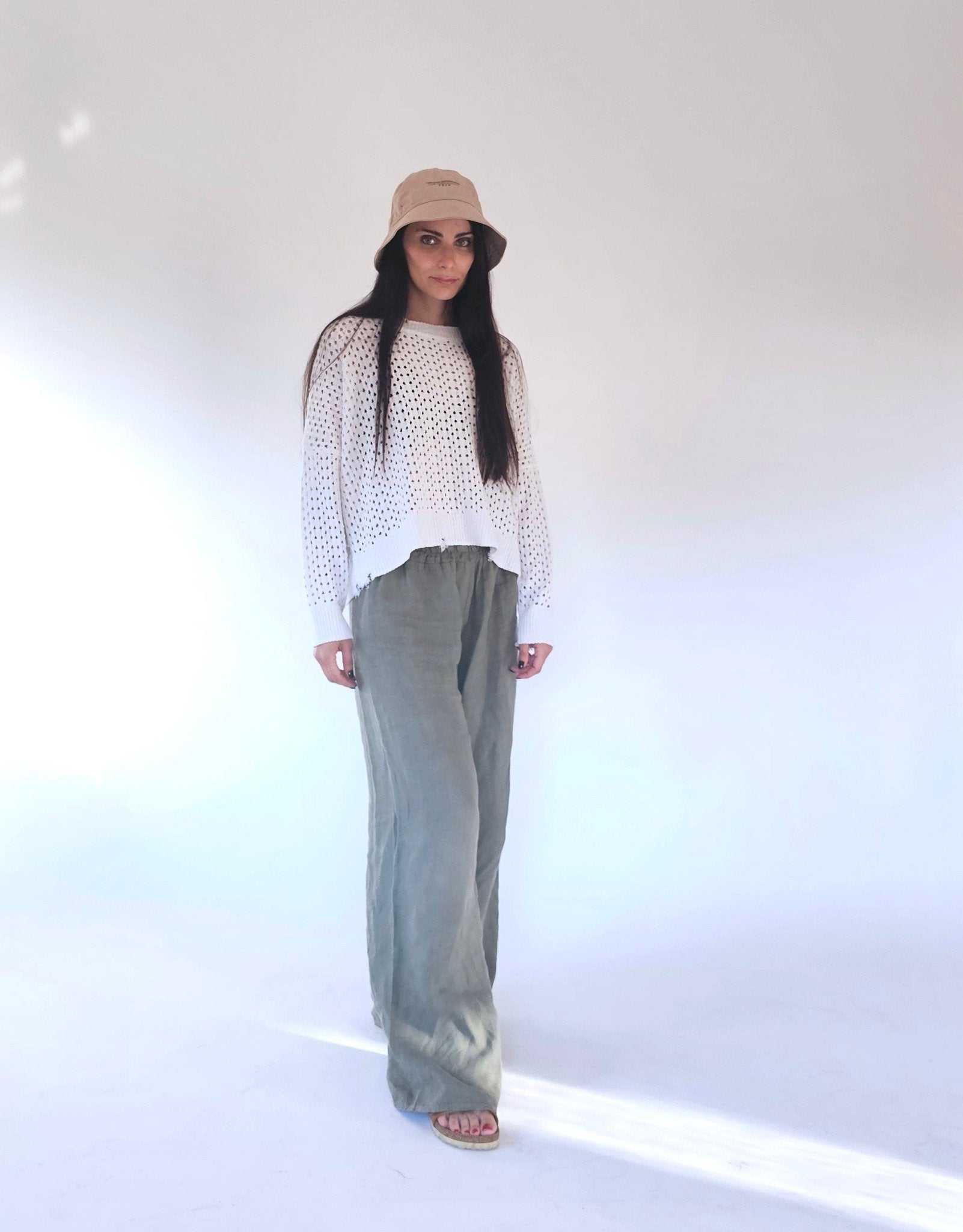 White open-knit cotton sweater by Tenné with fringed hem, paired with relaxed green trousers. Ideal for spring/summer layering.