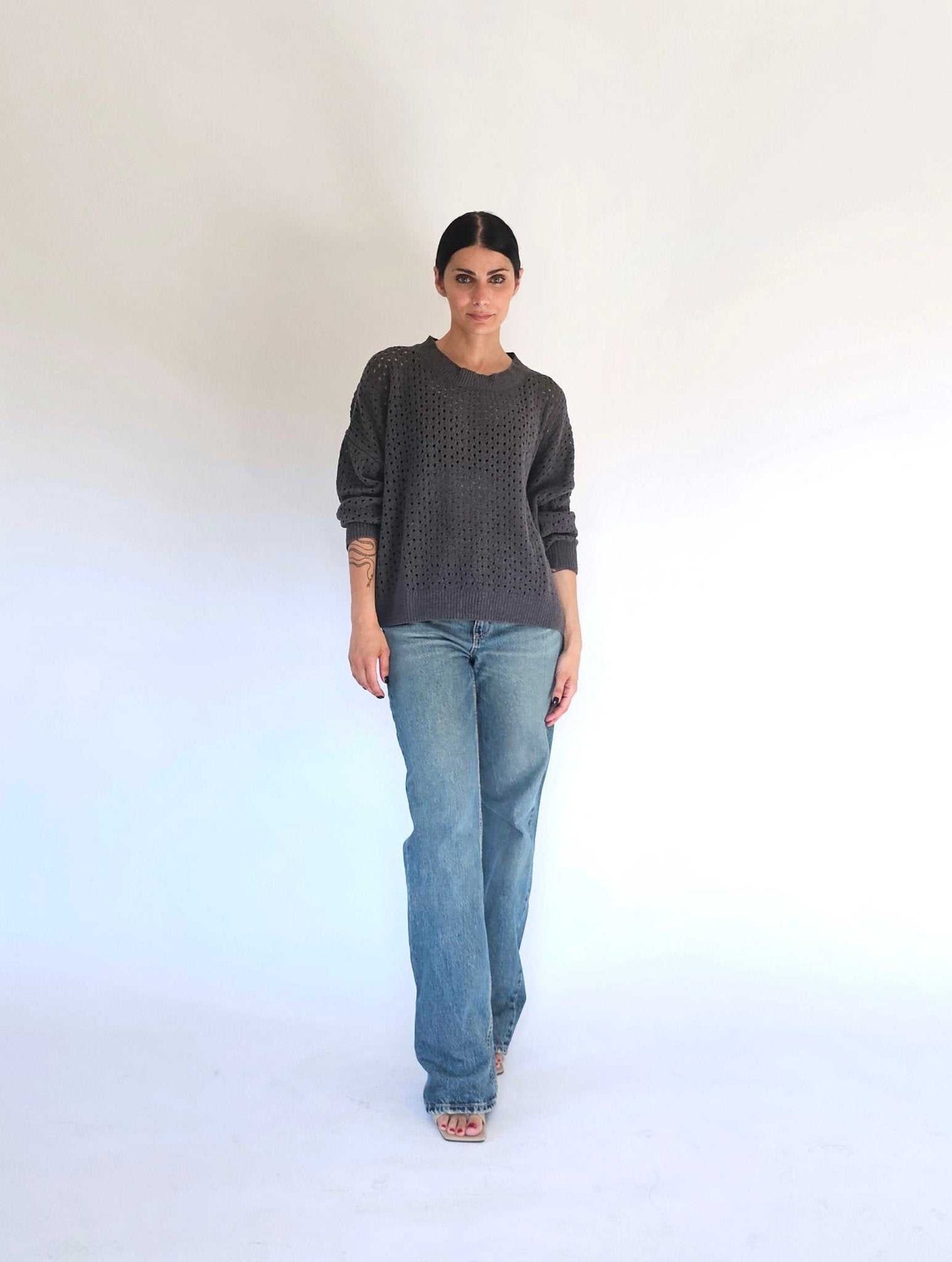 Charcoal version of Fabiana open-knit cotton sweater by Tenné, styled with blue jeans. Recycled cotton knitwear for casual wear.