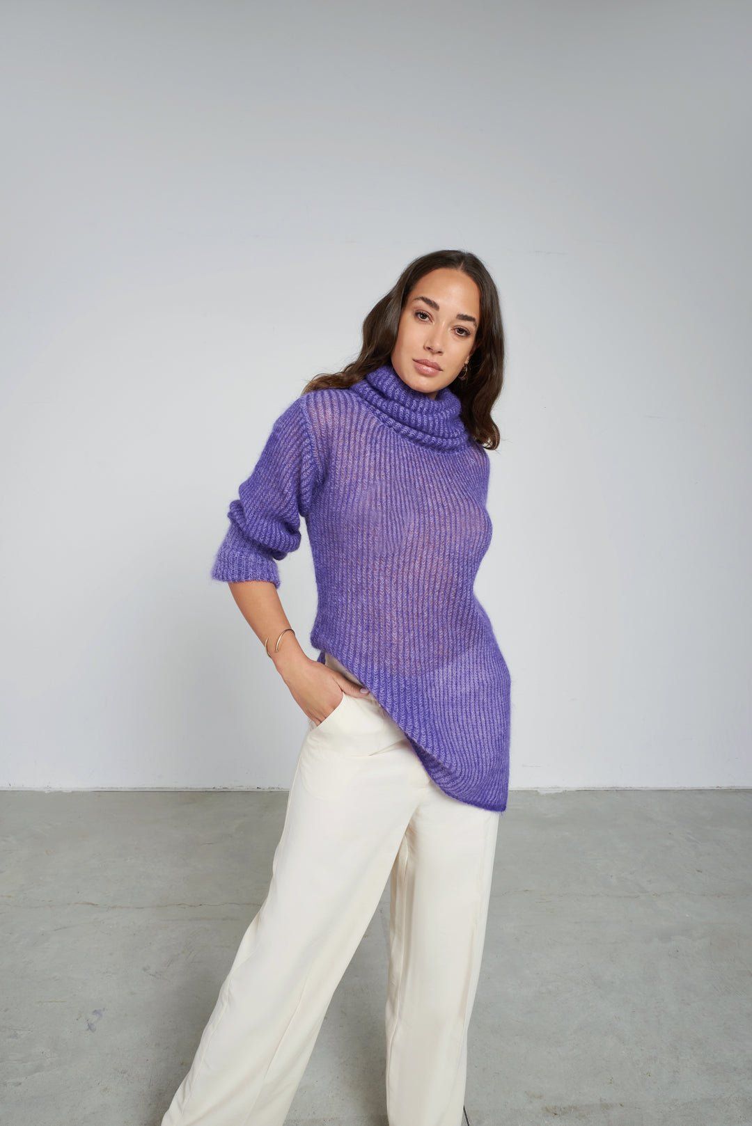 Nina by Tenné oversized wool alpaca sweater in purple with extra-high neck and side slits, styled with white trousers for autumn/winter fashion.