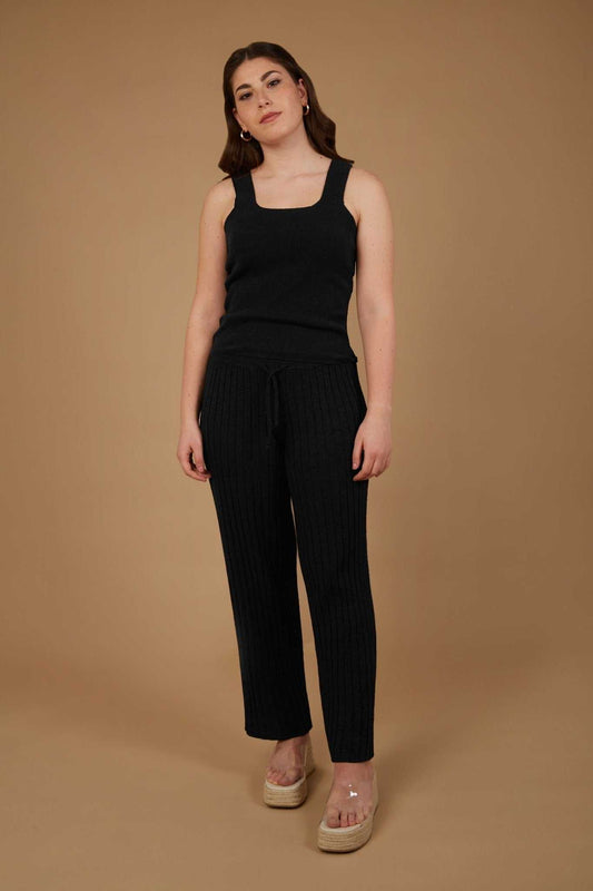 Margaret Tank Top - Sustainable Lyocell Tank Top in black shown on model against beige background, paired with ribbed knit pants for a sleek look.