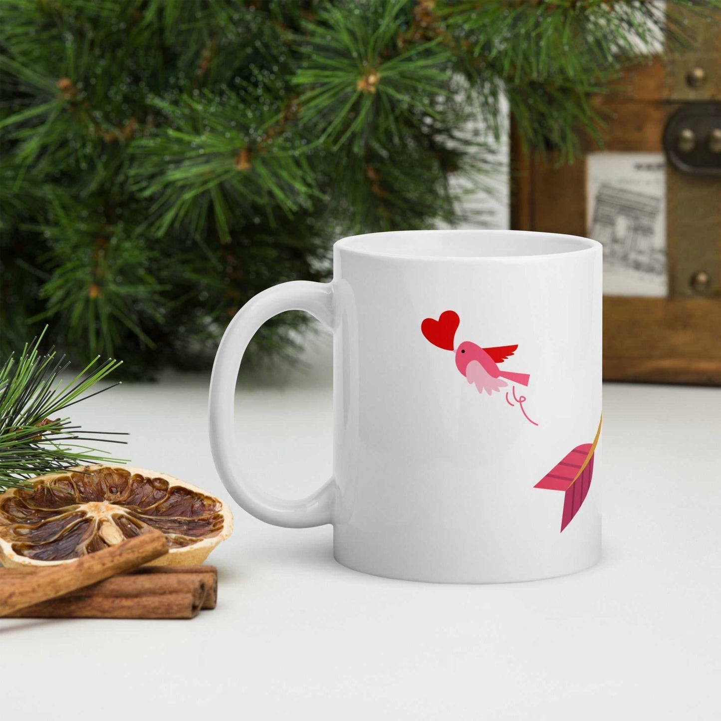Valentine mug gift featuring a pink bird with heart and arrow design, surrounded by festive greenery and cinnamon sticks.