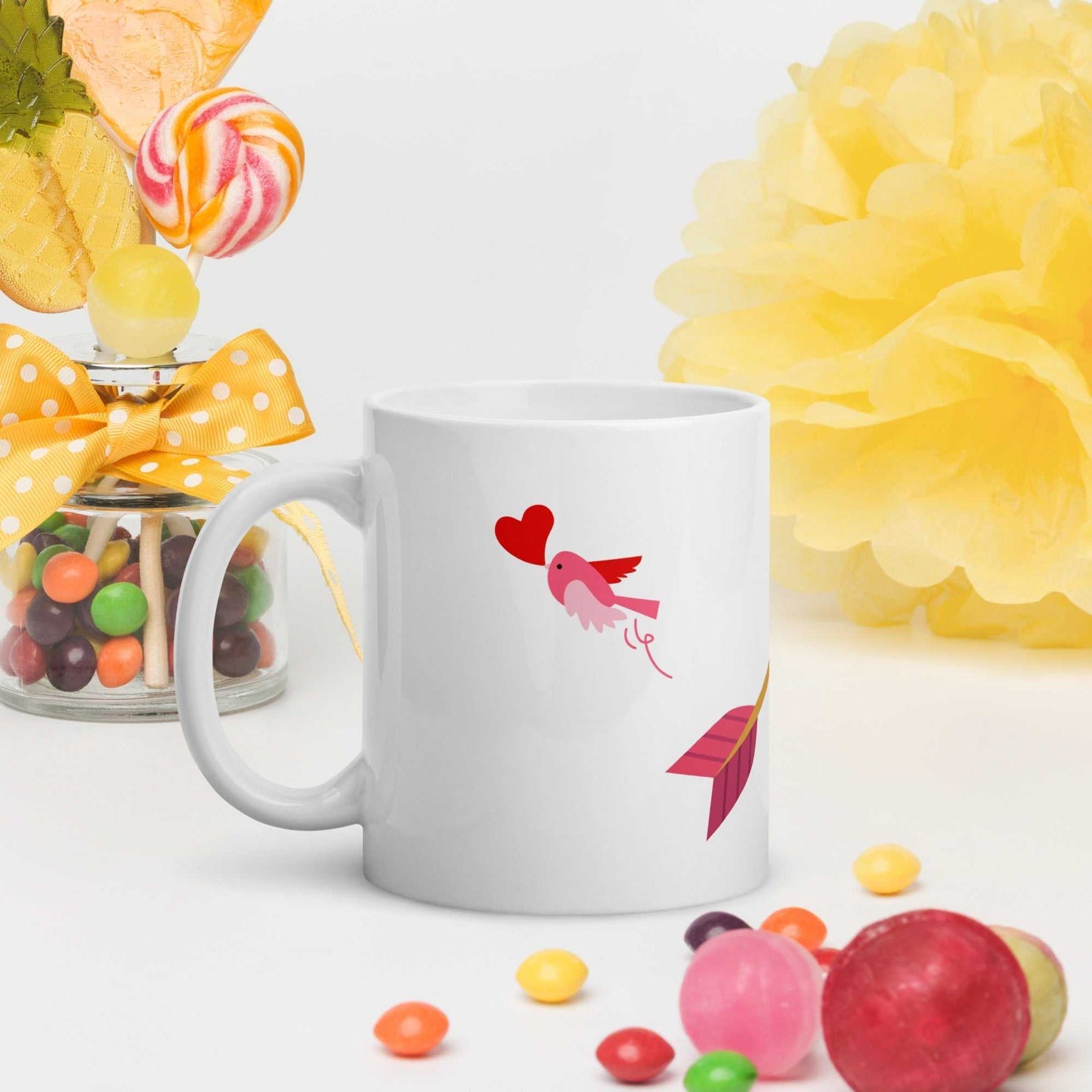Valentine mug gift with pink bird and arrow design, styled with colorful candy and festive yellow decor for gifting.