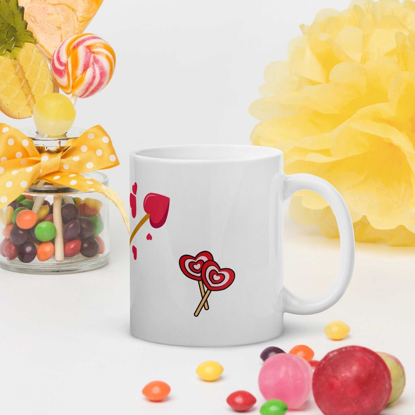 Valentine mug gift with heart lollipops and arrow design, surrounded by candy and cheerful yellow decorations.