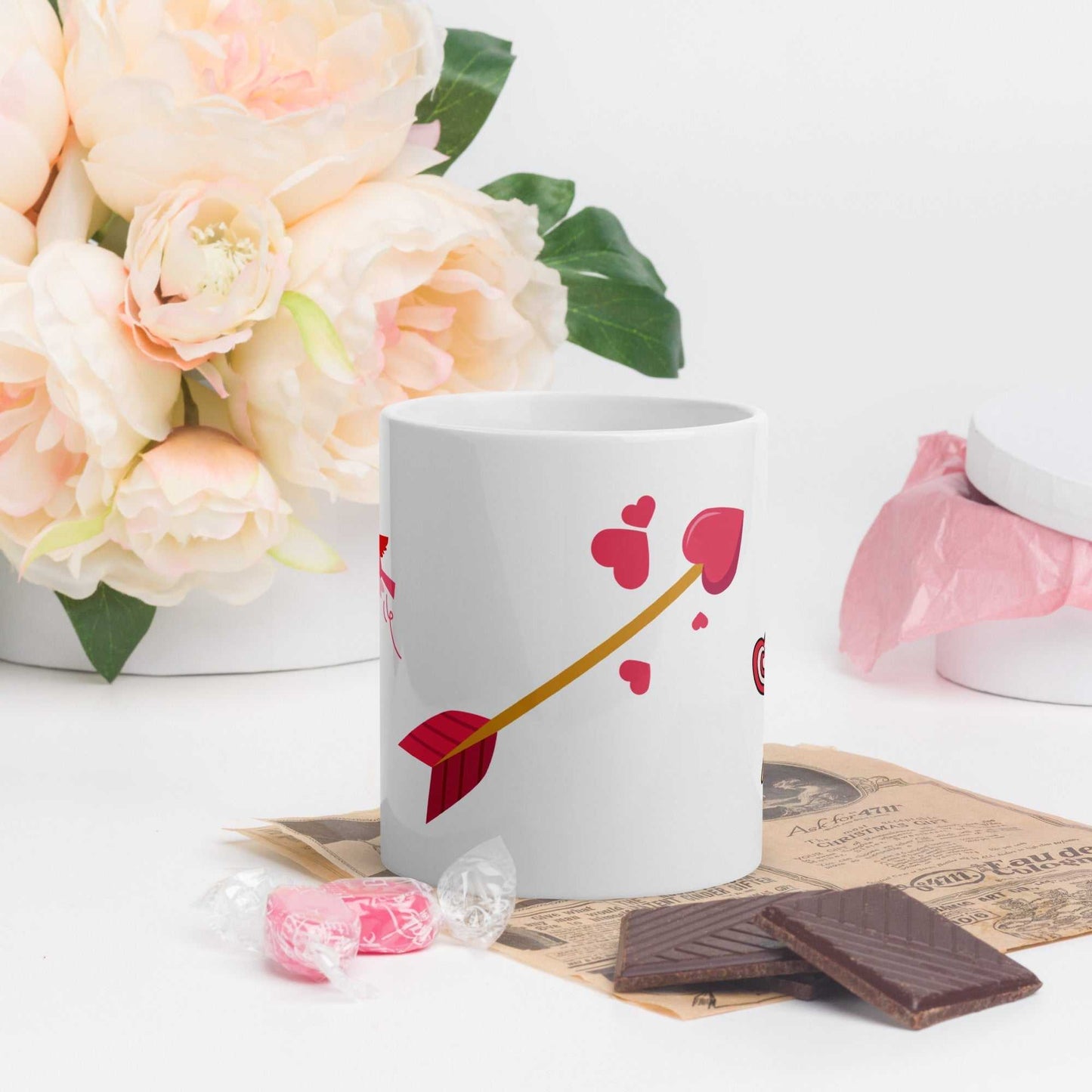 Valentine mug gift showing red heart arrow design, surrounded by chocolates and floral decor for a romantic vibe.