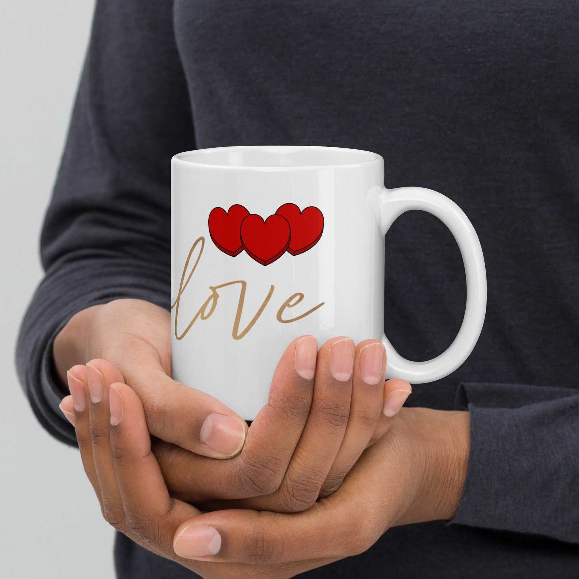 Hands holding ceramic valentine mug with red hearts and 'love' text, perfect romantic gift for coffee or tea lovers.