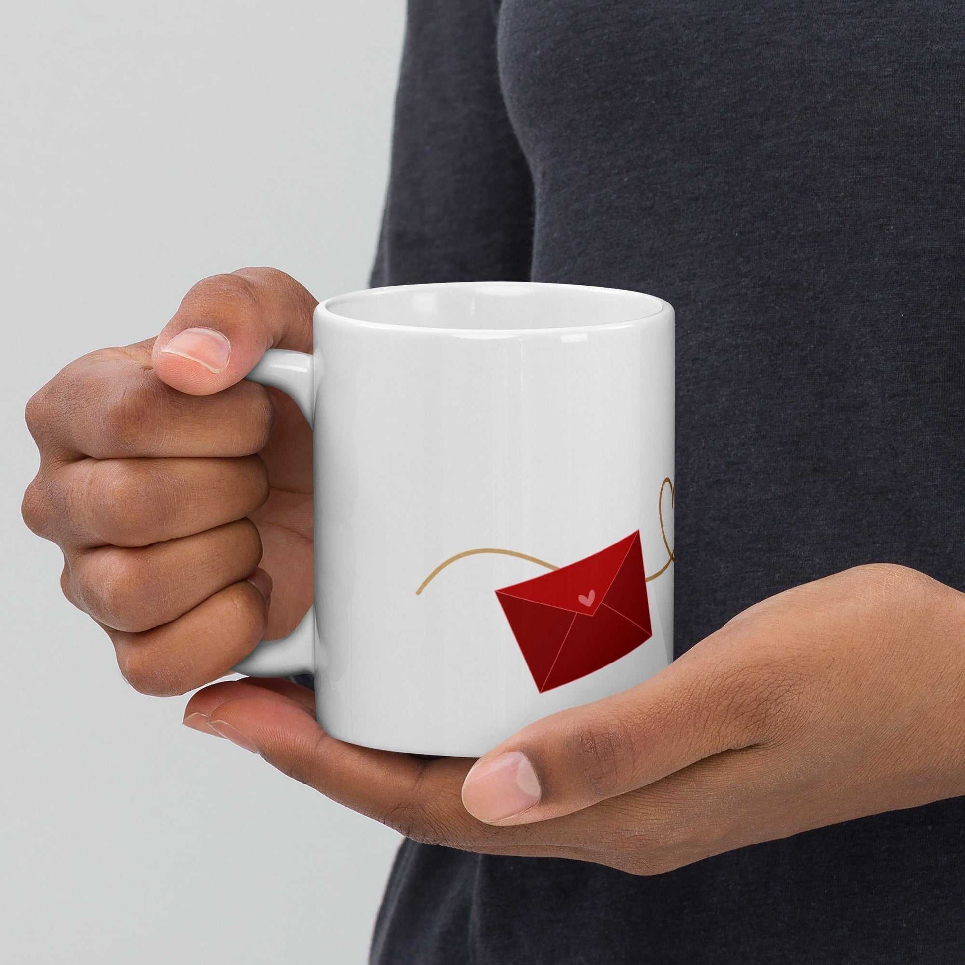 Close-up of hands holding valentine mug with red envelope design, ceramic and dishwasher safe, ideal for gifting.