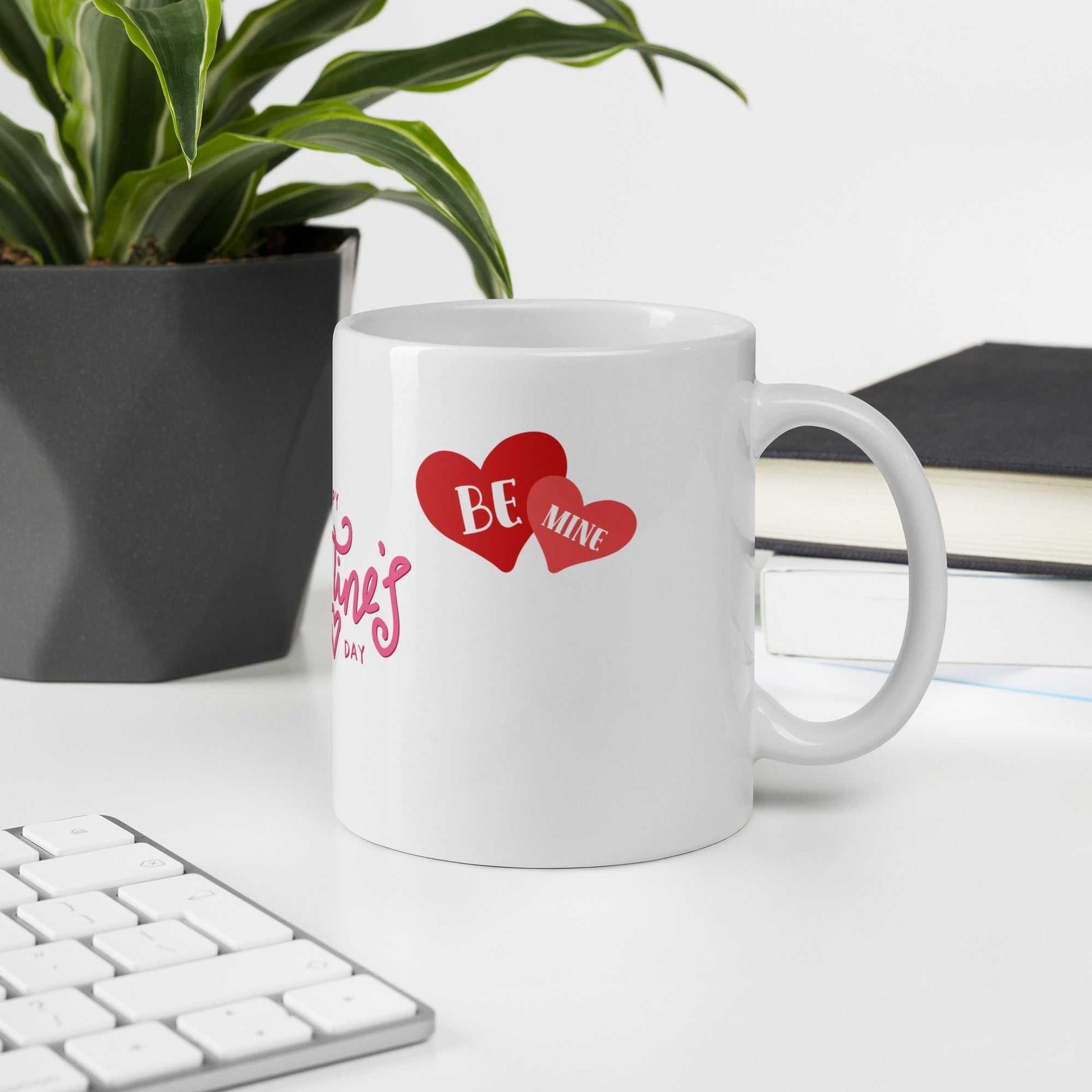 Valentine Mug - valentine mug | 11oz ceramic drinkware with 'Be Mine' heart design, placed on office desk near plant and keyboard.