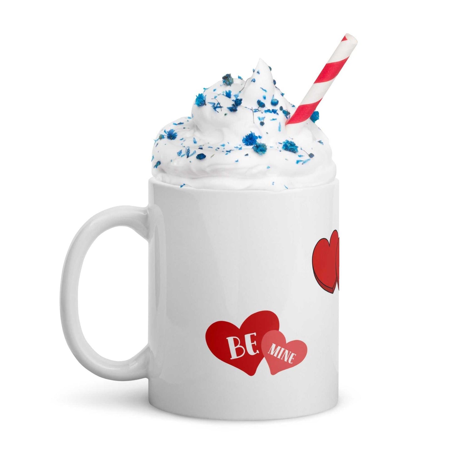 Valentine mug with 'Be Mine' heart design filled with whipped cream and blue sprinkles, ideal for festive hot drinks.