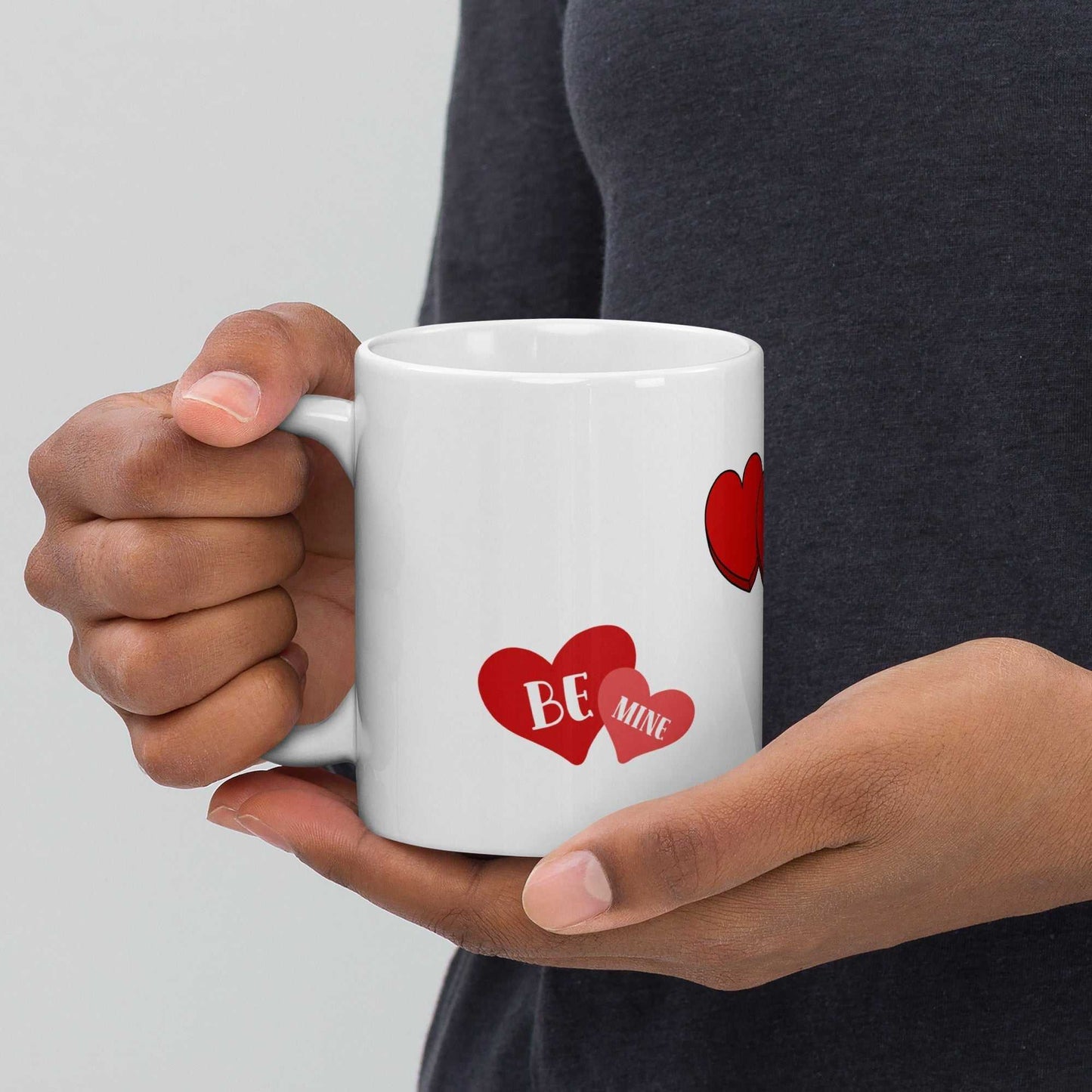 Hands holding ceramic Valentine mug with 'Be Mine' heart design, ideal for cozy romantic moments or gifting.
