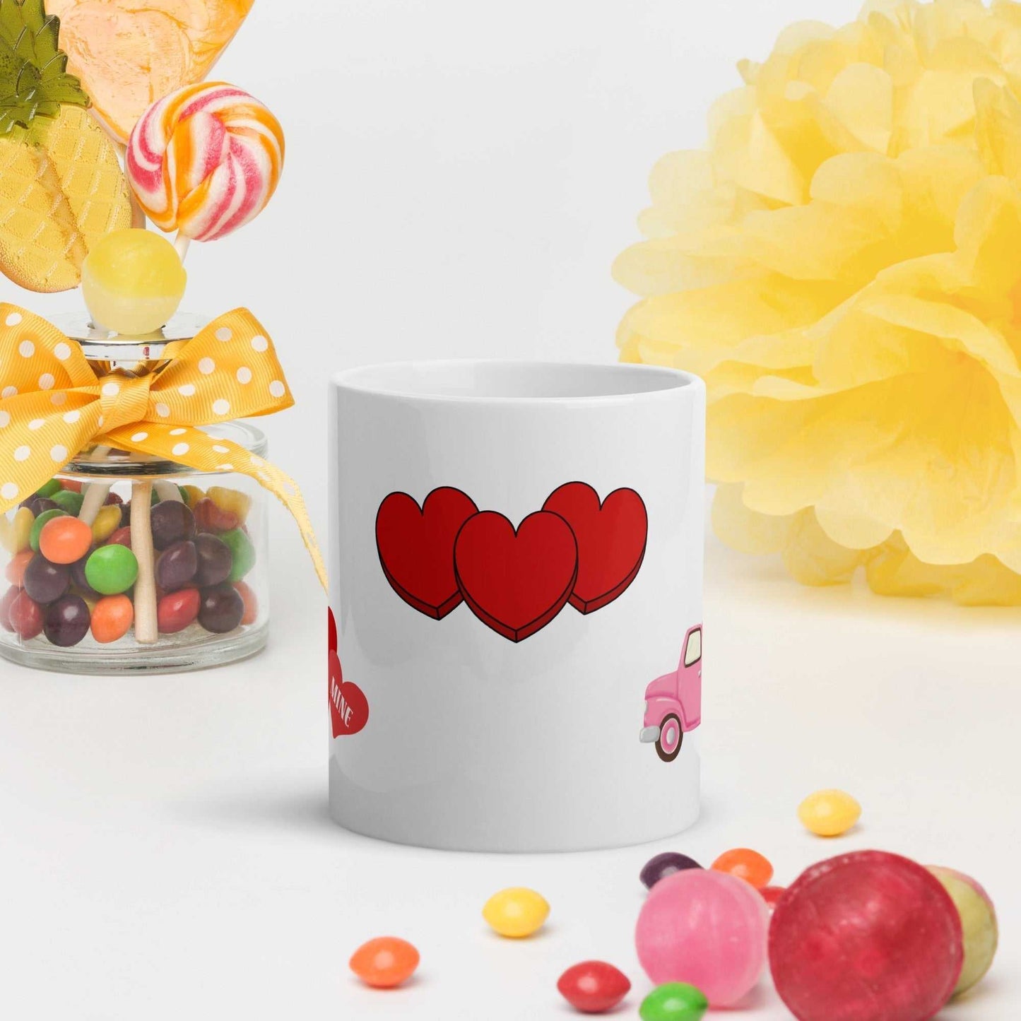 Valentine mug featuring three red hearts, styled with colorful candy and yellow background, perfect for romantic occasions.