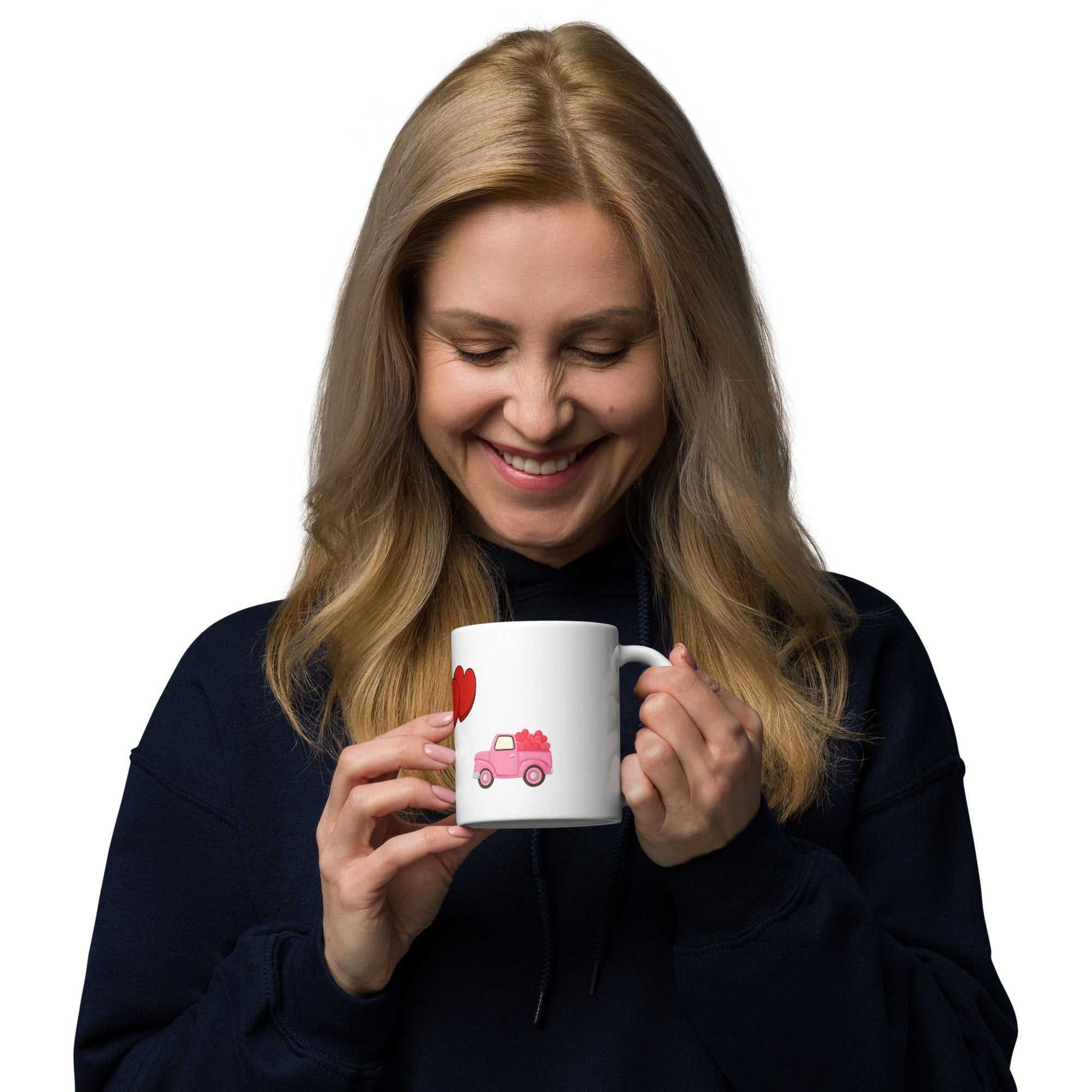 Woman smiling while holding Valentine mug with pink truck and hearts, 11 oz ceramic ideal for love-themed gifts.