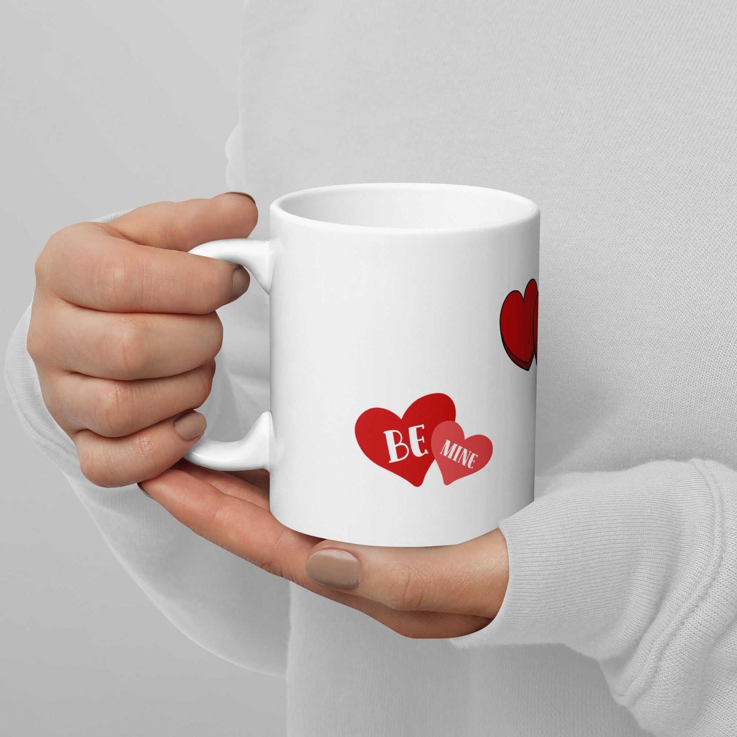 Close-up of hands holding white Valentine mug with red hearts and 'Be Mine' text, perfect for Valentine's Day gifts.