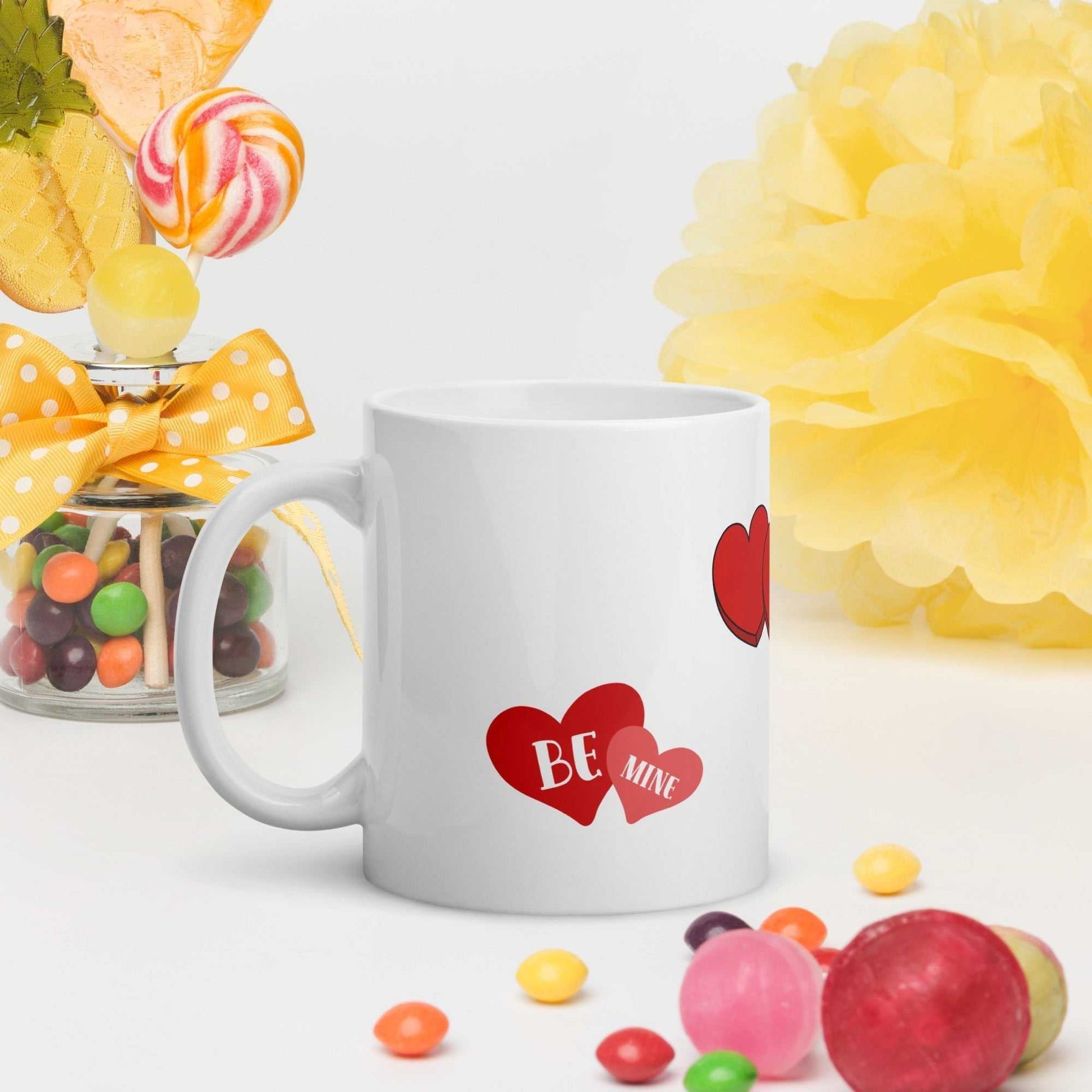Valentine mug with 'Be Mine' heart design, surrounded by colorful candy and festive decor, ideal for romantic celebrations.
