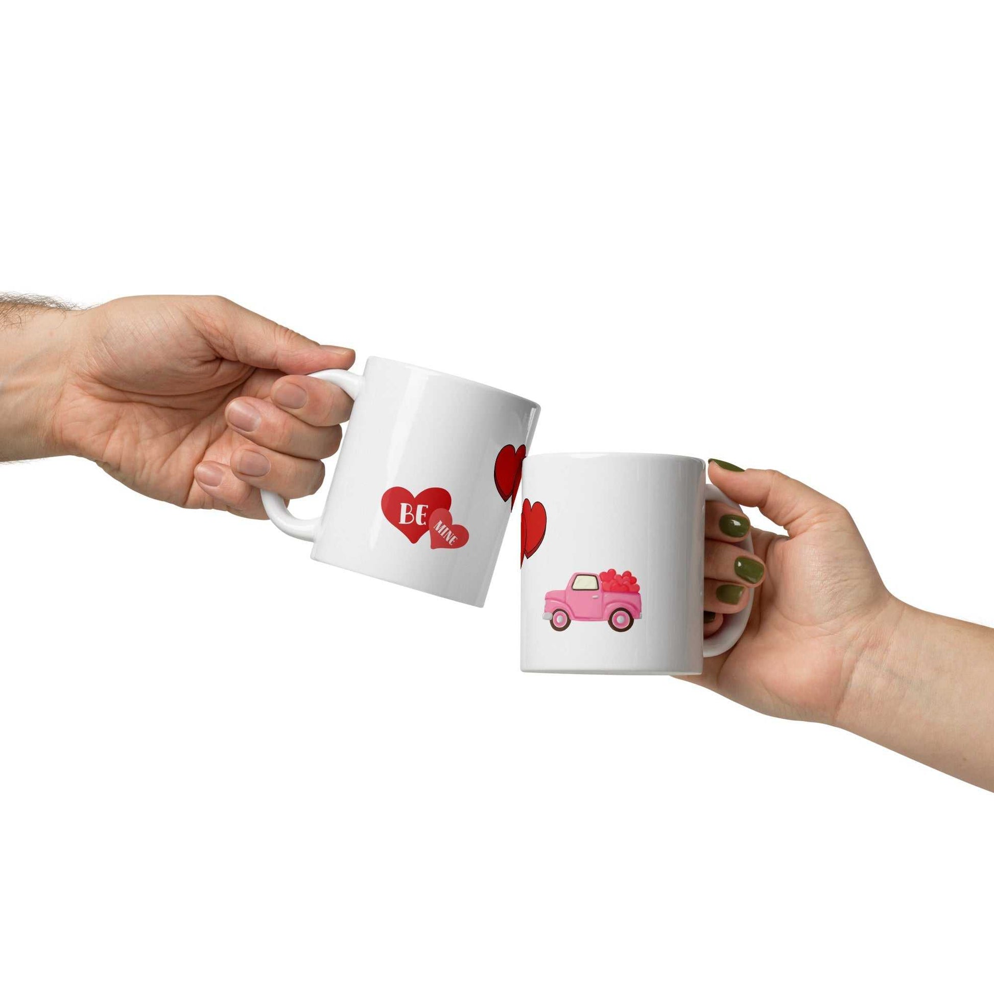 Two people clinking Valentine mugs with heart and pink truck design, celebrating love with themed drinkware.